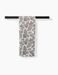 The Danelys Sidron Autumn Pines towel, featuring green oak leaves and brown acorns on white ultra-absorbent Geoweave fabric, hangs on a black horizontal towel bar against a plain white background.