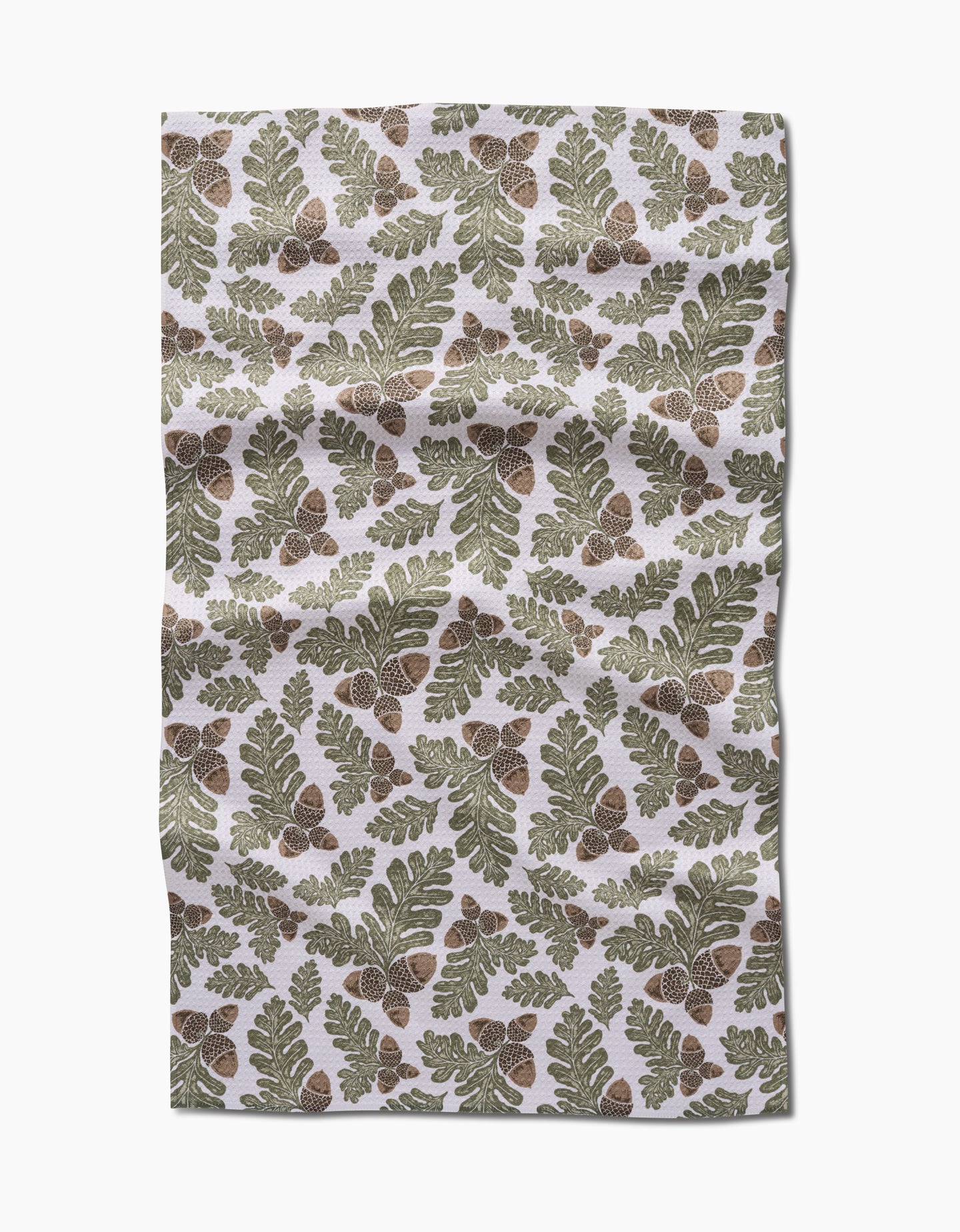 Autumn Pines by Danelys Sidron is an ultra-absorbent Geoweave fabric with a repeating pattern of green oak leaves and brown acorns on a white background. The fabric has a slightly wrinkled appearance.