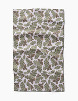 Autumn Pines by Danelys Sidron is an ultra-absorbent Geoweave fabric with a repeating pattern of green oak leaves and brown acorns on a white background. The fabric has a slightly wrinkled appearance.