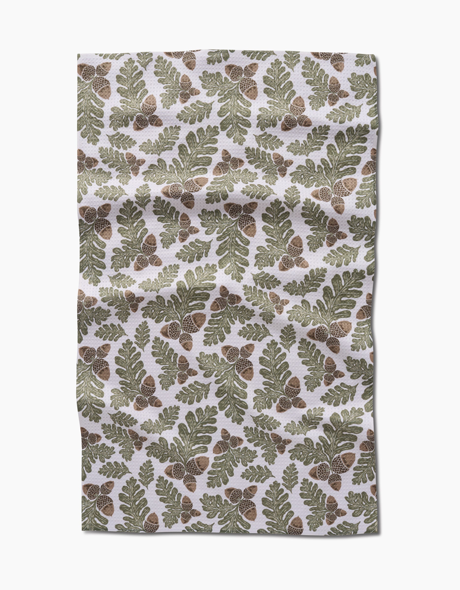 Autumn Pines by Danelys Sidron is an ultra-absorbent Geoweave fabric with a repeating pattern of green oak leaves and brown acorns on a white background. The fabric has a slightly wrinkled appearance.