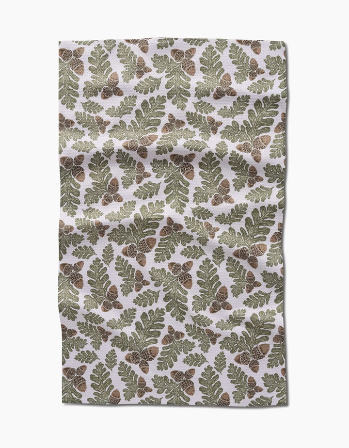 Autumn Pines by Danelys Sidron is an ultra-absorbent Geoweave fabric with a repeating pattern of green oak leaves and brown acorns on a white background. The fabric has a slightly wrinkled appearance.