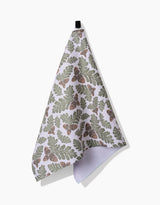 The Autumn Pines kitchen towel by Danelys Sidron is made from ultra-absorbent Geoweave fabric, featuring a green and brown oak leaf and acorn pattern and a black hanging loop, shown against a plain white background.