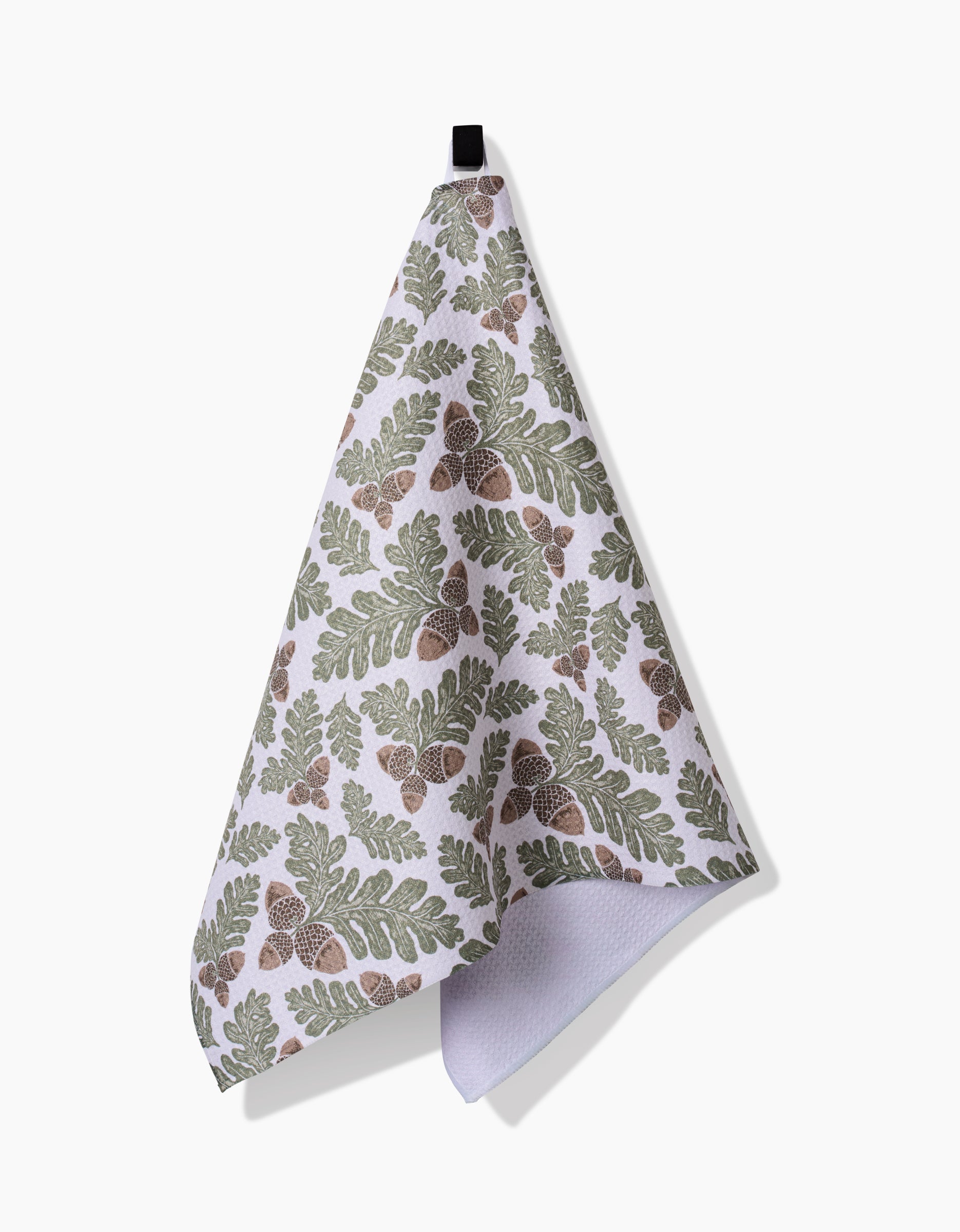 The Autumn Pines kitchen towel by Danelys Sidron is made from ultra-absorbent Geoweave fabric, featuring a green and brown oak leaf and acorn pattern and a black hanging loop, shown against a plain white background.