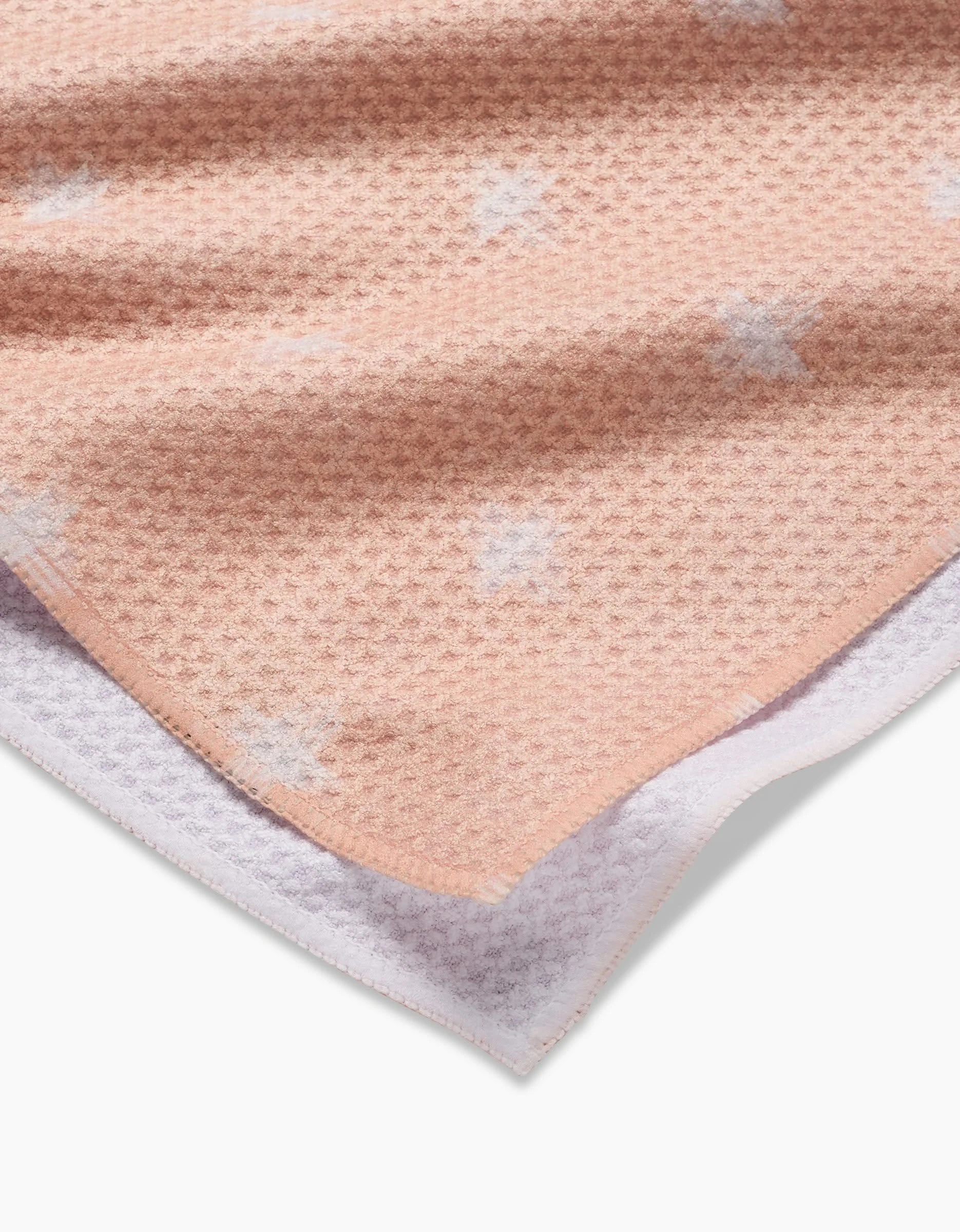 A close-up of the Aveline Tea Towel by Amy MacCready, featuring peach-colored Geoweave fabric with a waffle weave and small white crosses, hemmed edges, and a glimpse of the white underside.