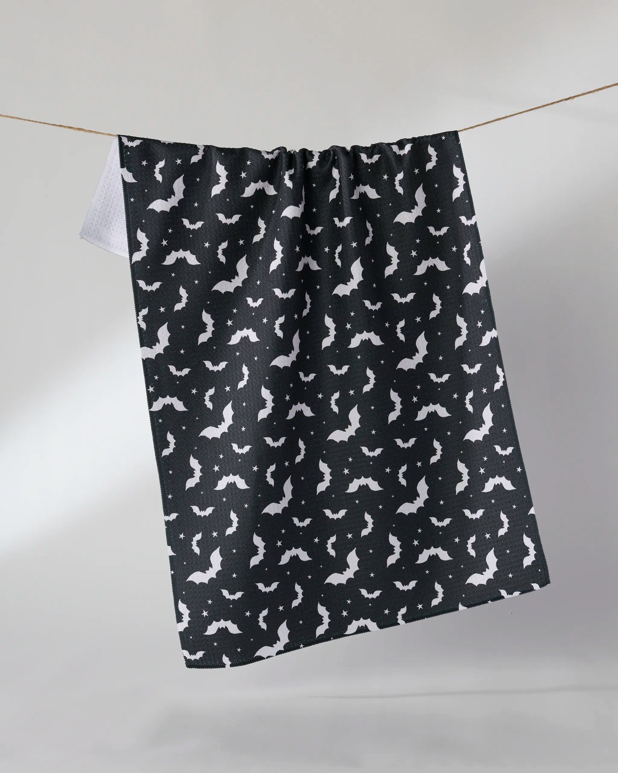 The Geometry “Batty Night” black tea towel with white bat silhouettes hangs on a clothesline against a light background.
