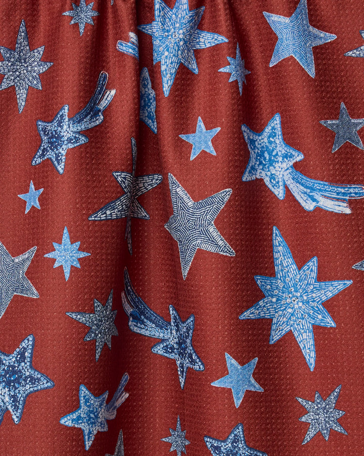The Geometry Beaded Stars tea towel features a maroon backdrop with blue and white stars in various sizes and patterns, crafted from ultra-absorbent recycled materials.