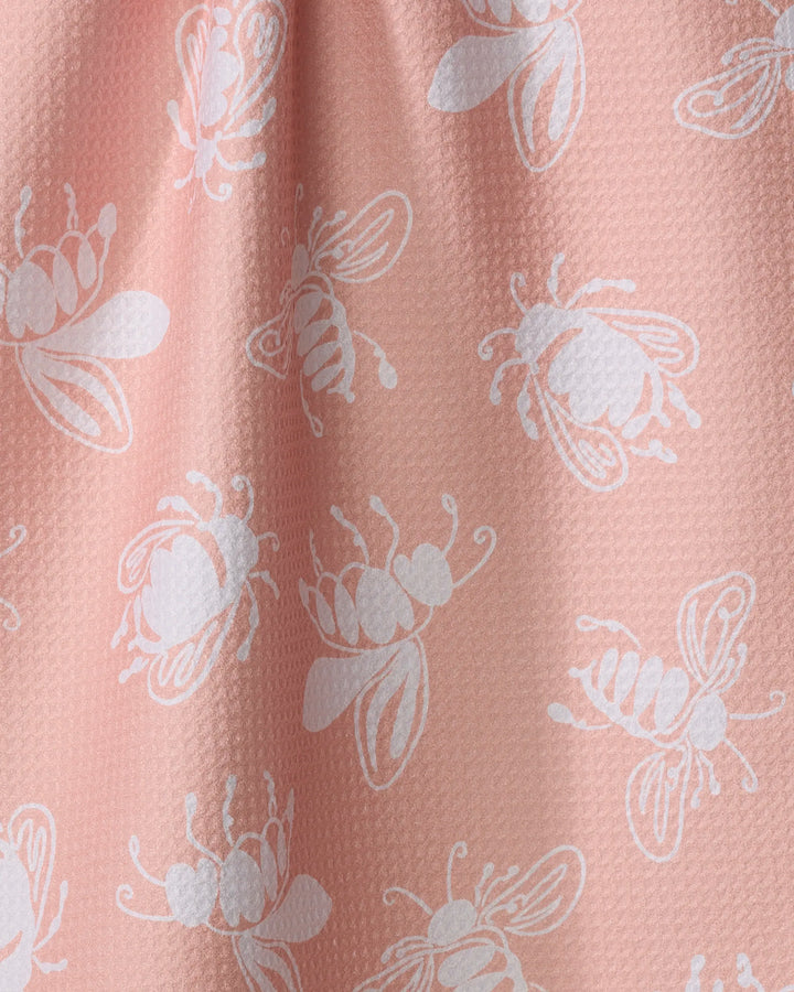 A close-up of the Sara Mari "Beelieve" pink tea towel, made from recycled materials and featuring a subtle raised texture with a repeating white, stylized bee pattern.