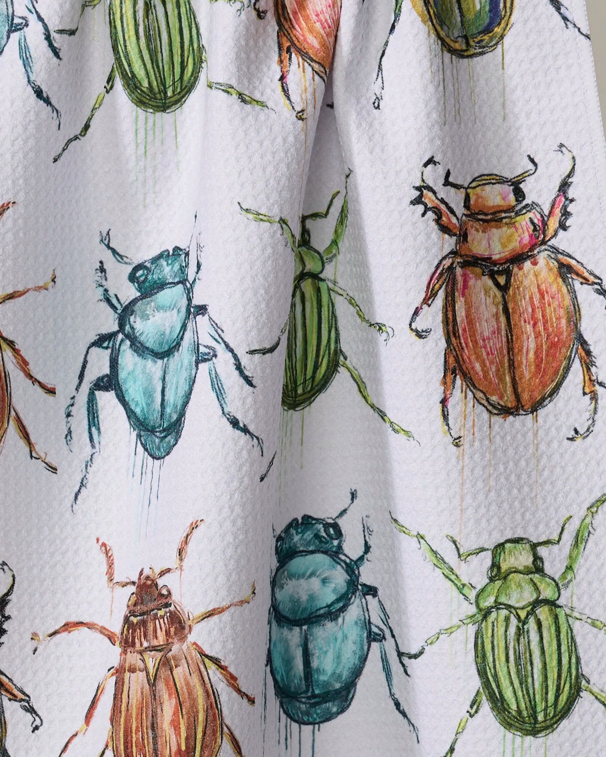 The Beetles tea towel by Taryn Brennan is white and textured, featuring a repeating pattern of colorful beetles in green, blue, brown, and orange, illustrated with watercolor-style details.