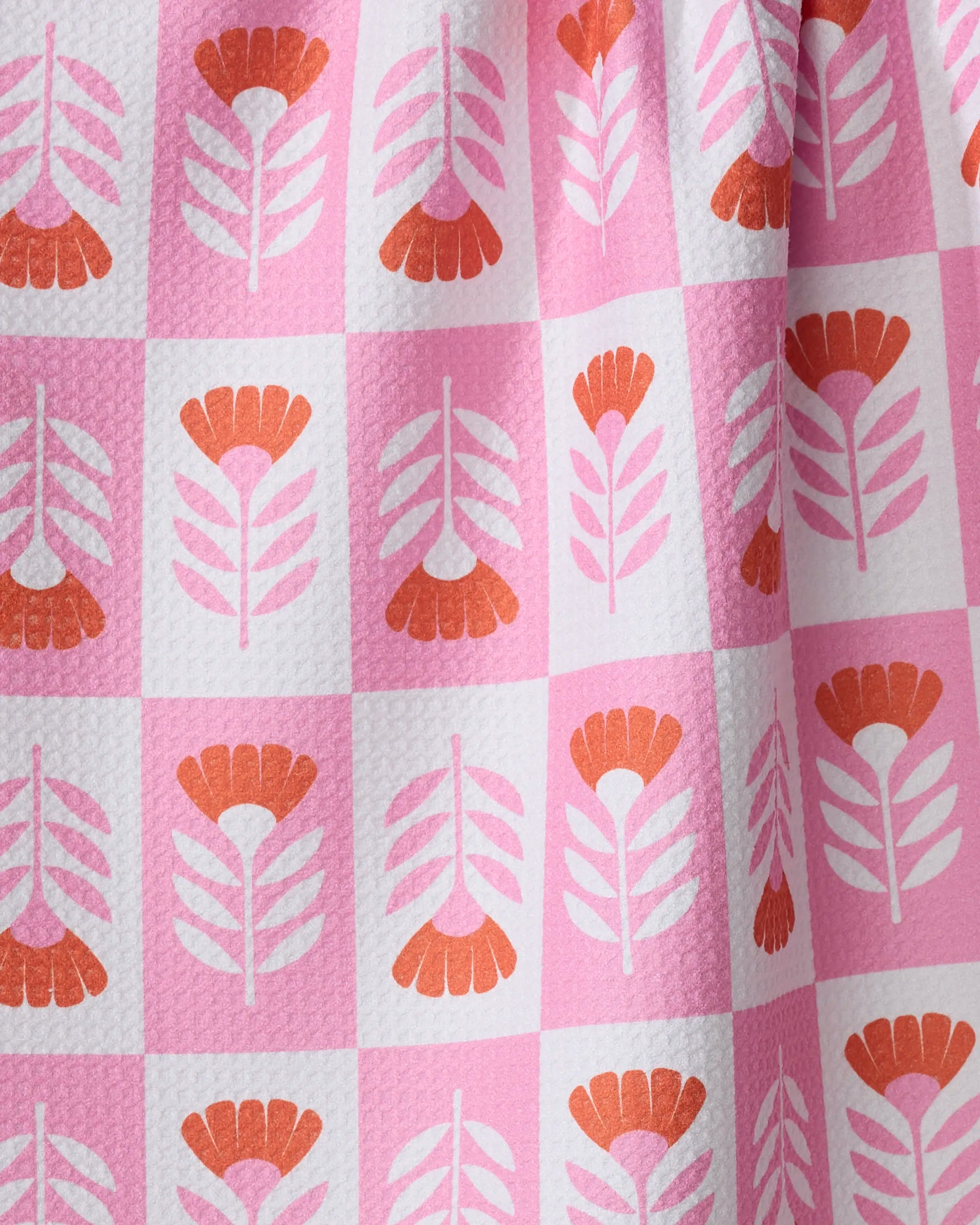 A close-up of the Charlie Rowan Designs Berry Flower Patch kitchen towel, featuring a pink and white checkered pattern with pink and orange floral designs in each square on textured recycled fabric.