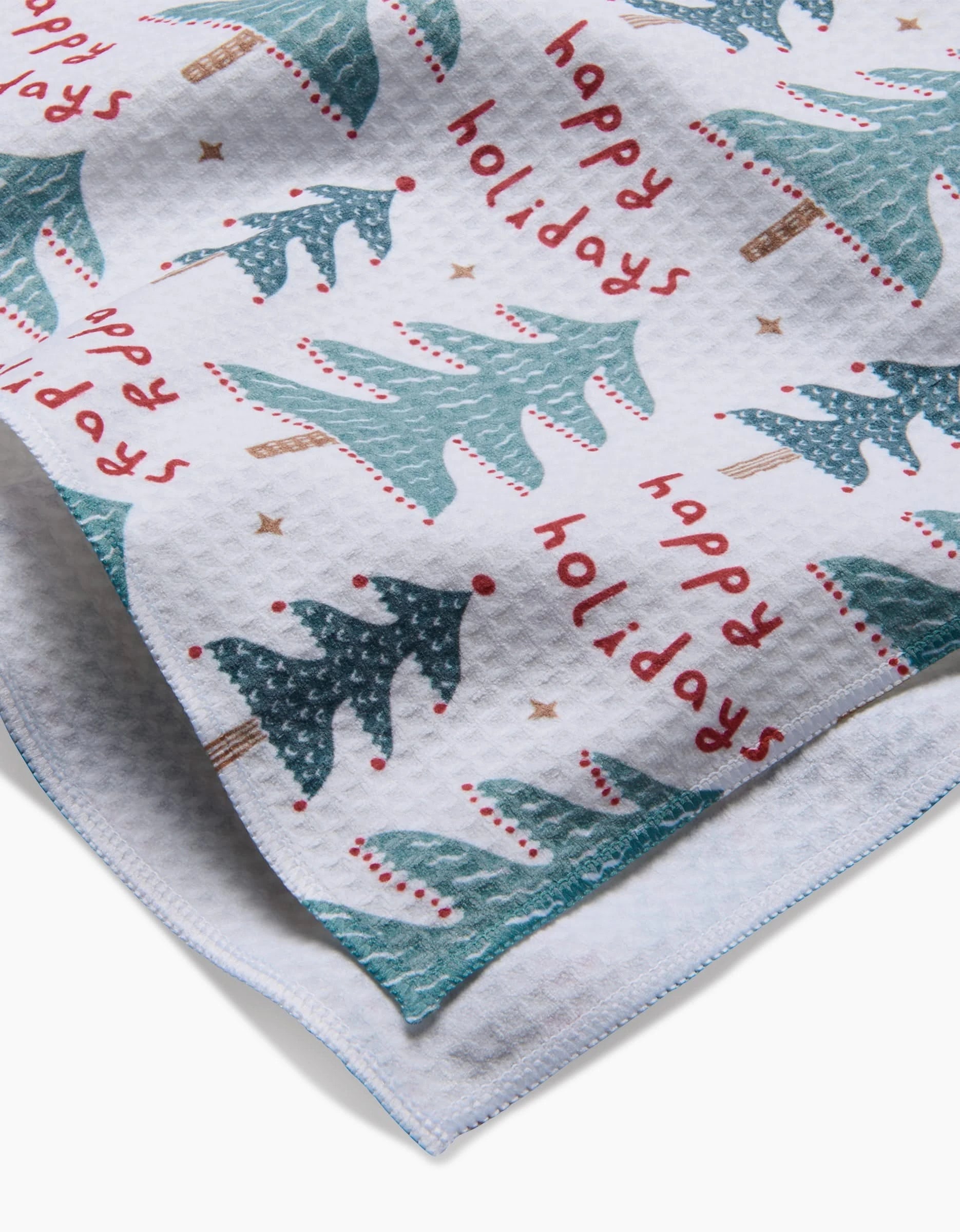 The Berry Happy Holidays tea towel by Roxy Marj features green Christmas trees, red ornaments, and “happy holidays” on a textured white background—made from recycled materials for a festive and sustainable accent.