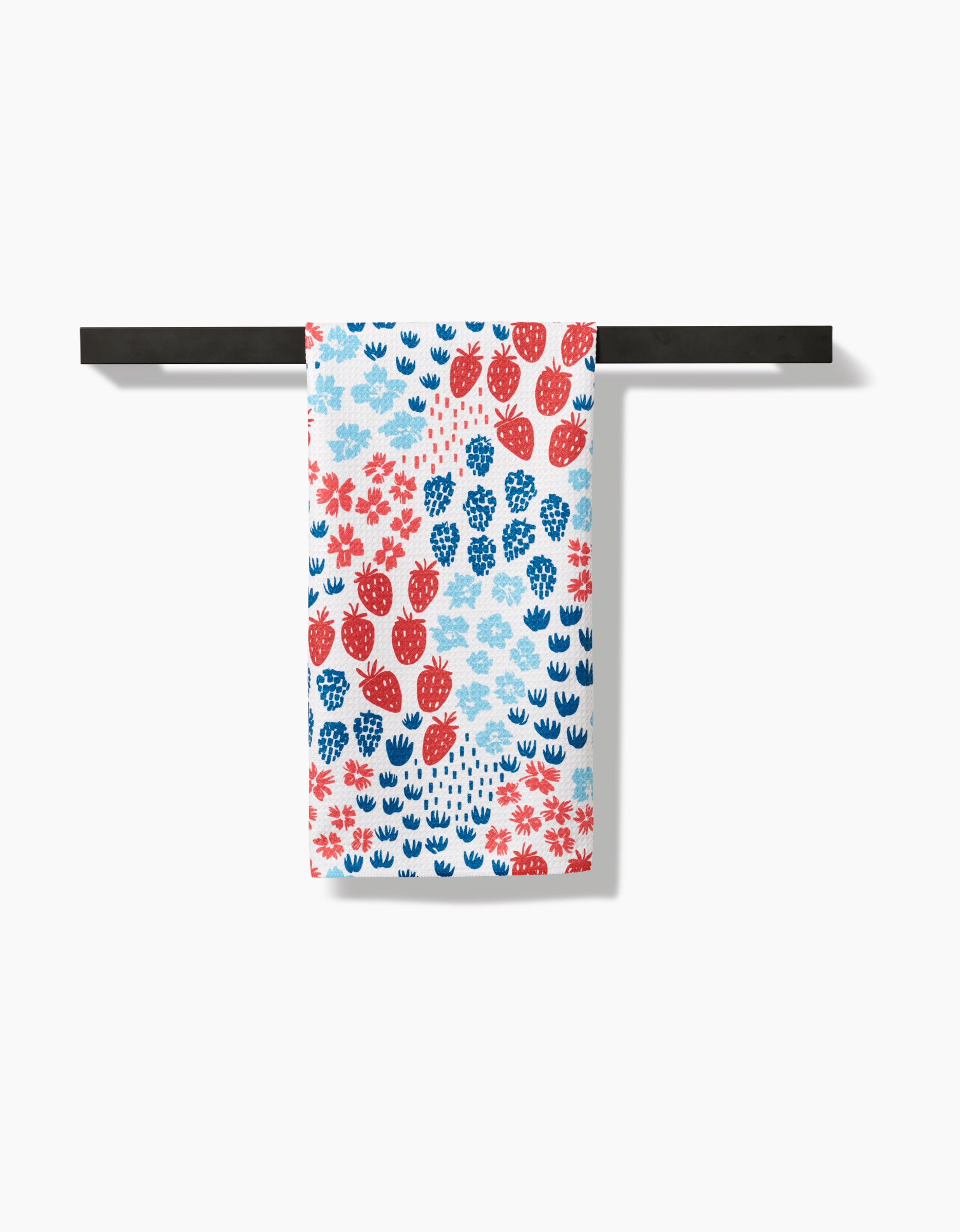 The Berry Meadow tea towel by Hufton Studio, featuring red and blue floral and leaf patterns, hangs neatly over a black bar. Crafted from premium Geoweave fabric, it is displayed against a plain white background.
