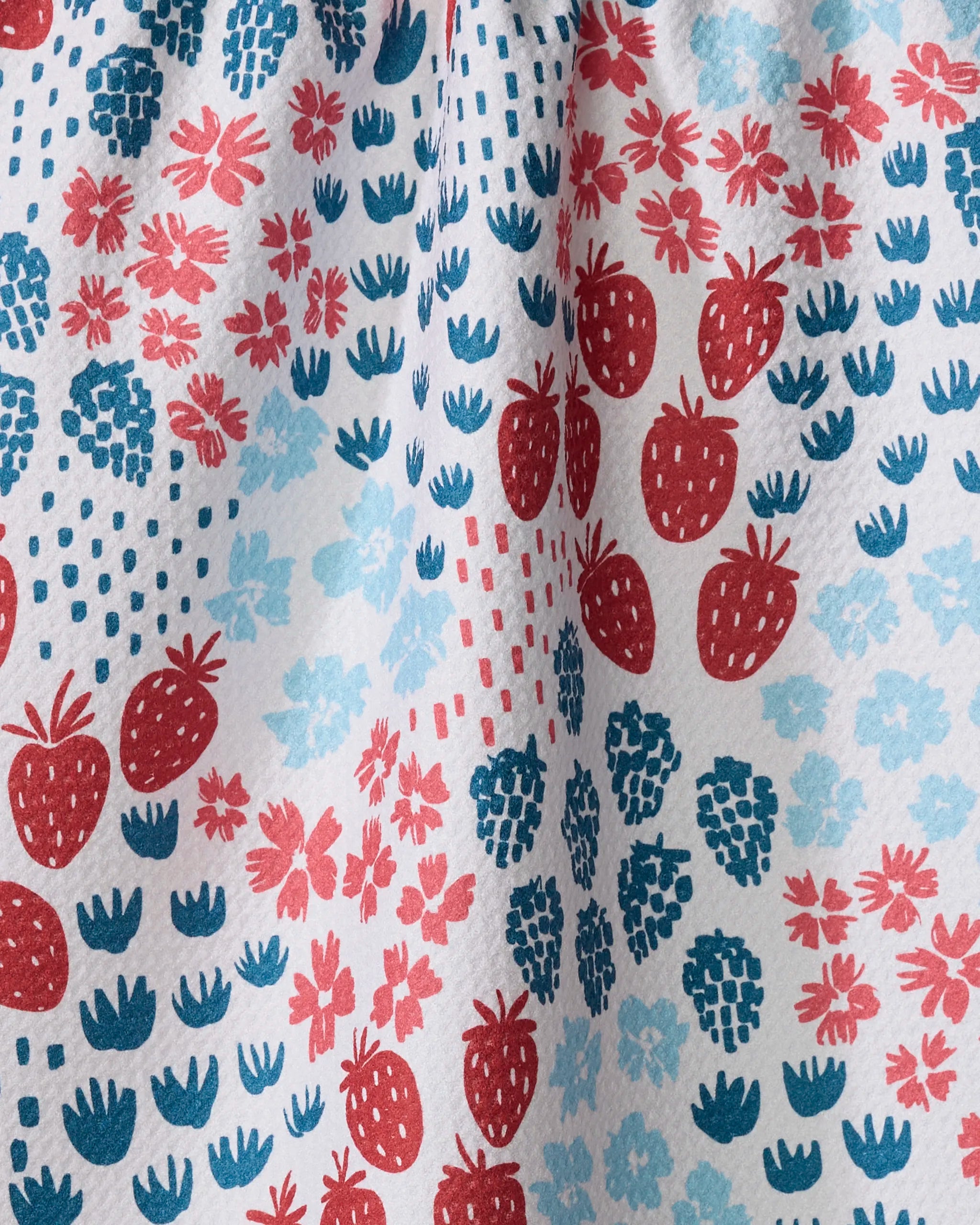A close-up of Hufton Studio's Berry Meadow ultra-absorbent towel, showcasing a colorful pattern of red strawberries, blue raspberries, and blue and red flower clusters on a white background.