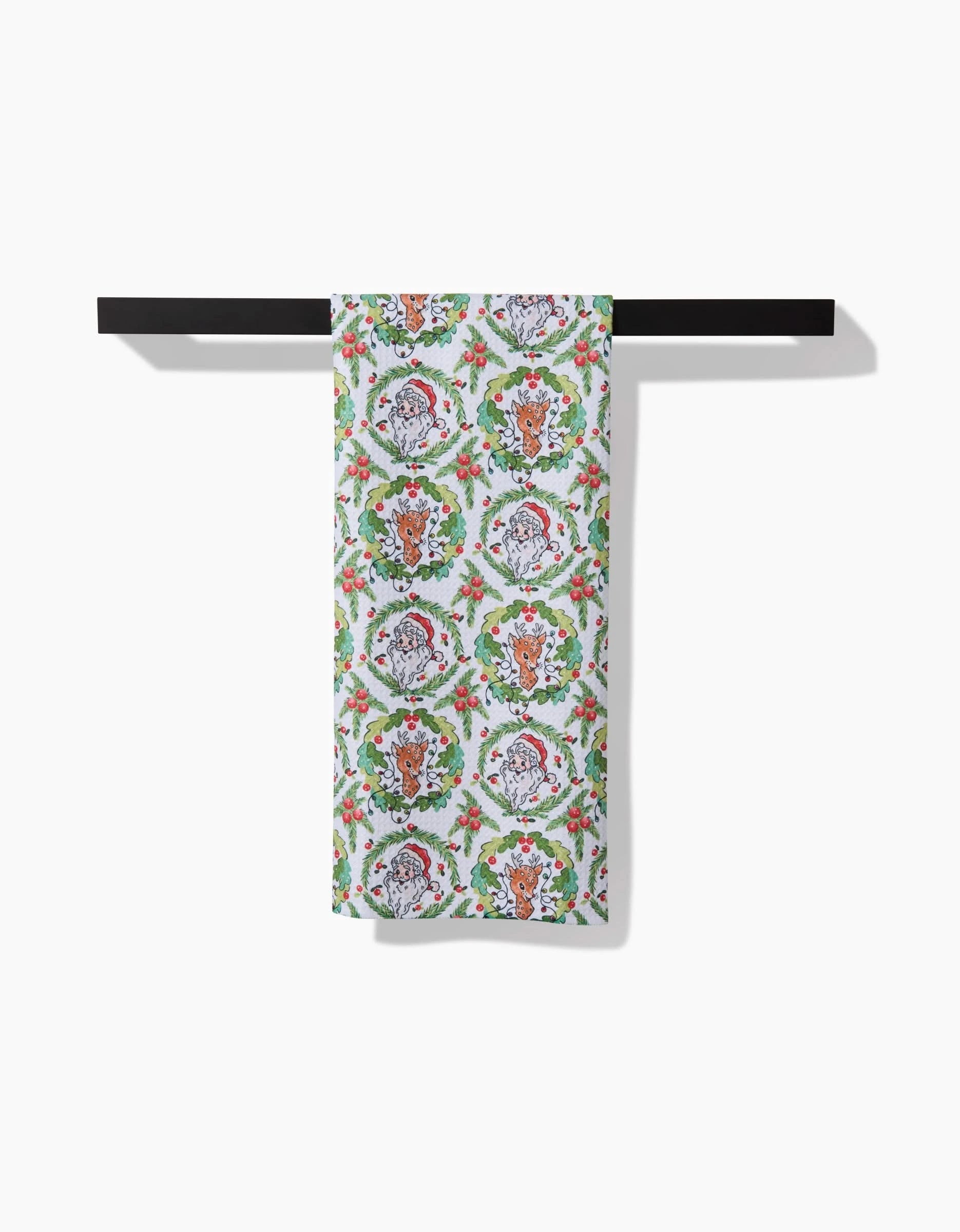 The Sara Mari Berry Retro Holiday kitchen towel, featuring a vibrant floral and animal design made from recycled materials, hangs neatly on a black rod against a white backdrop.