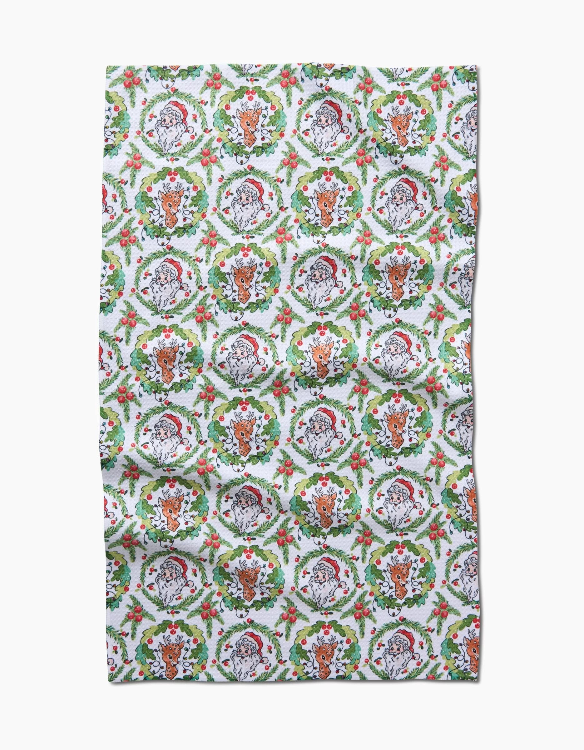 The Berry Retro Holiday tea towel by Sara Mari features repeating wreath designs with Santa and reindeer faces, holly berries, and green leaves on a white background—a festive touch for your kitchen this season.