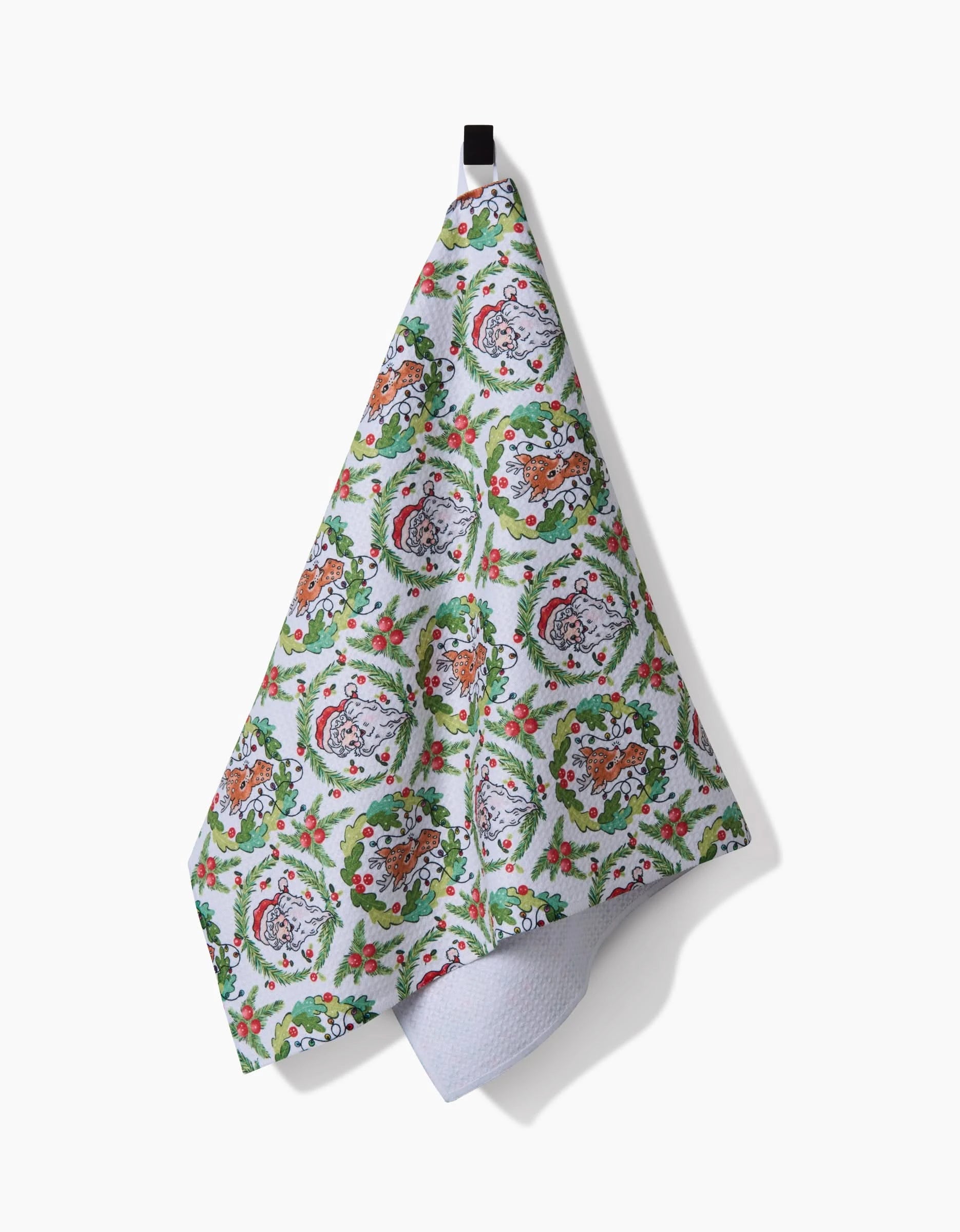 The Sara Mari Berry Retro Holiday tea towel features wreaths, holly, and cats in Santa hats. Hanging from a black loop against a white background, it brings festive cheer to any kitchen.