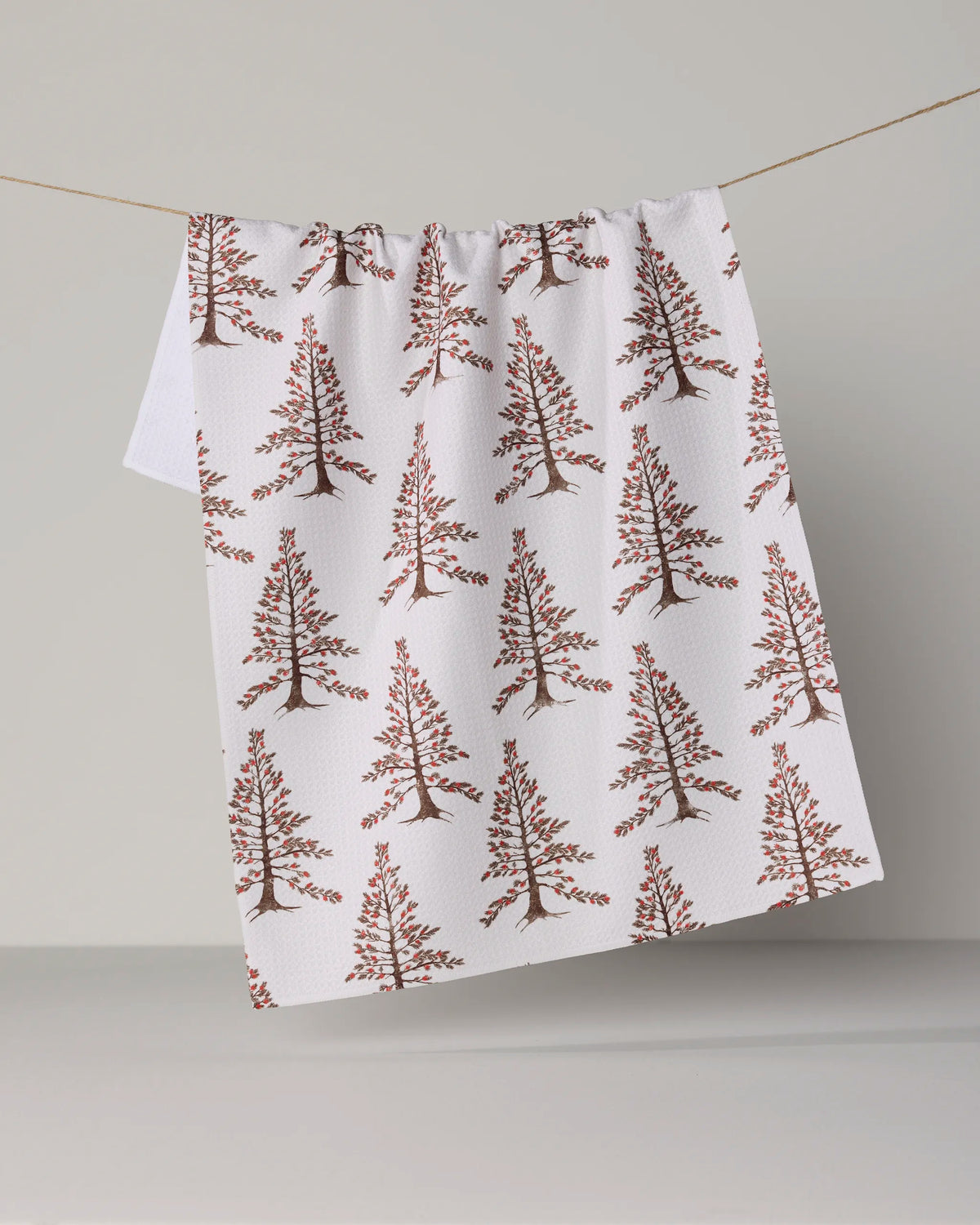 Berrywood by Geometry: An ultra-absorbent white tea towel featuring a repeating brown tree pattern, crafted from recycled materials for a stylish and sustainable touch. Shown hanging over a thin string against a plain light gray background.