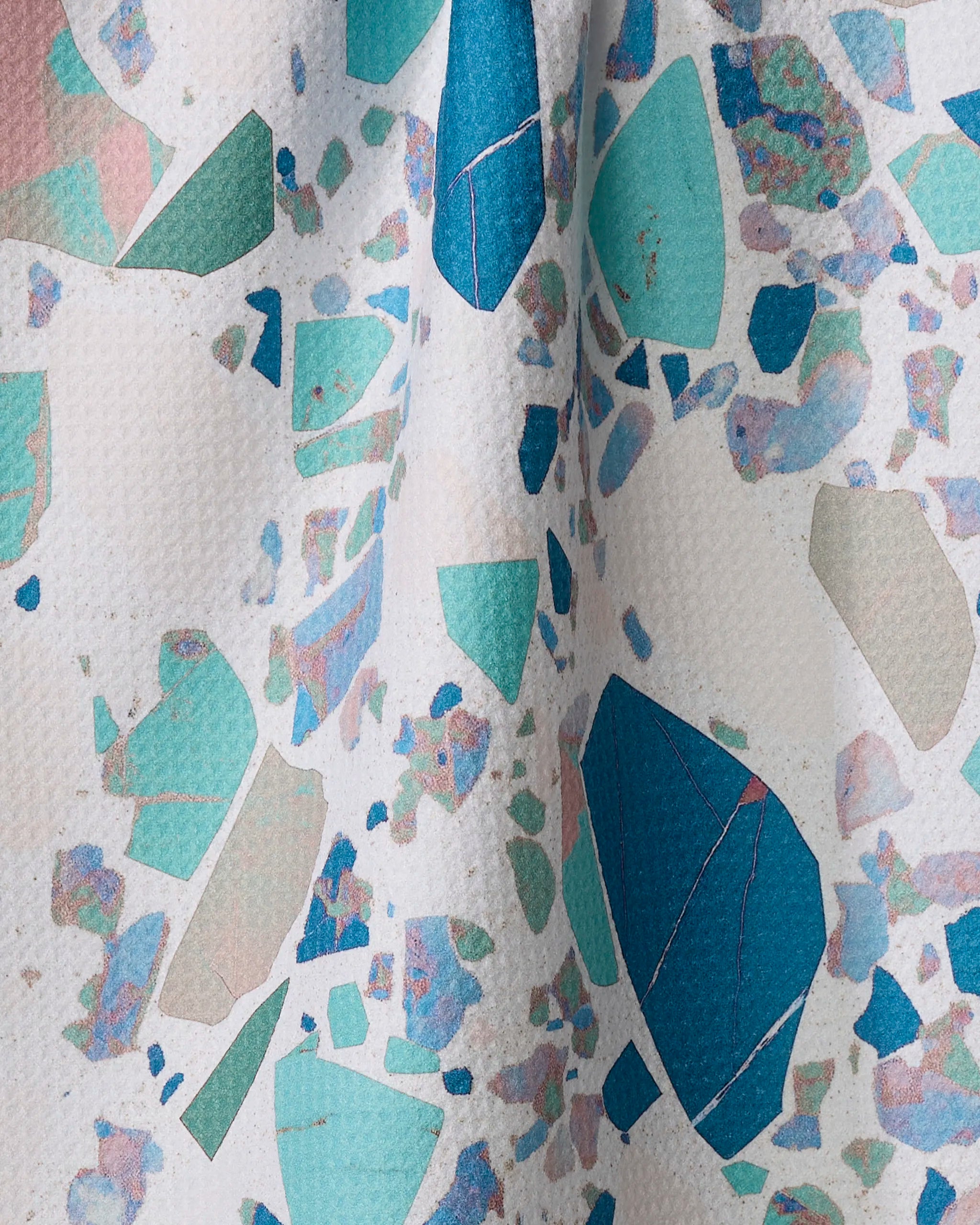 A close-up of Geometry's Beryl surface shows its terrazzo pattern—irregular blue, teal, mint, and light pink shapes on white—crafted from recycled materials for an eco-friendly touch.