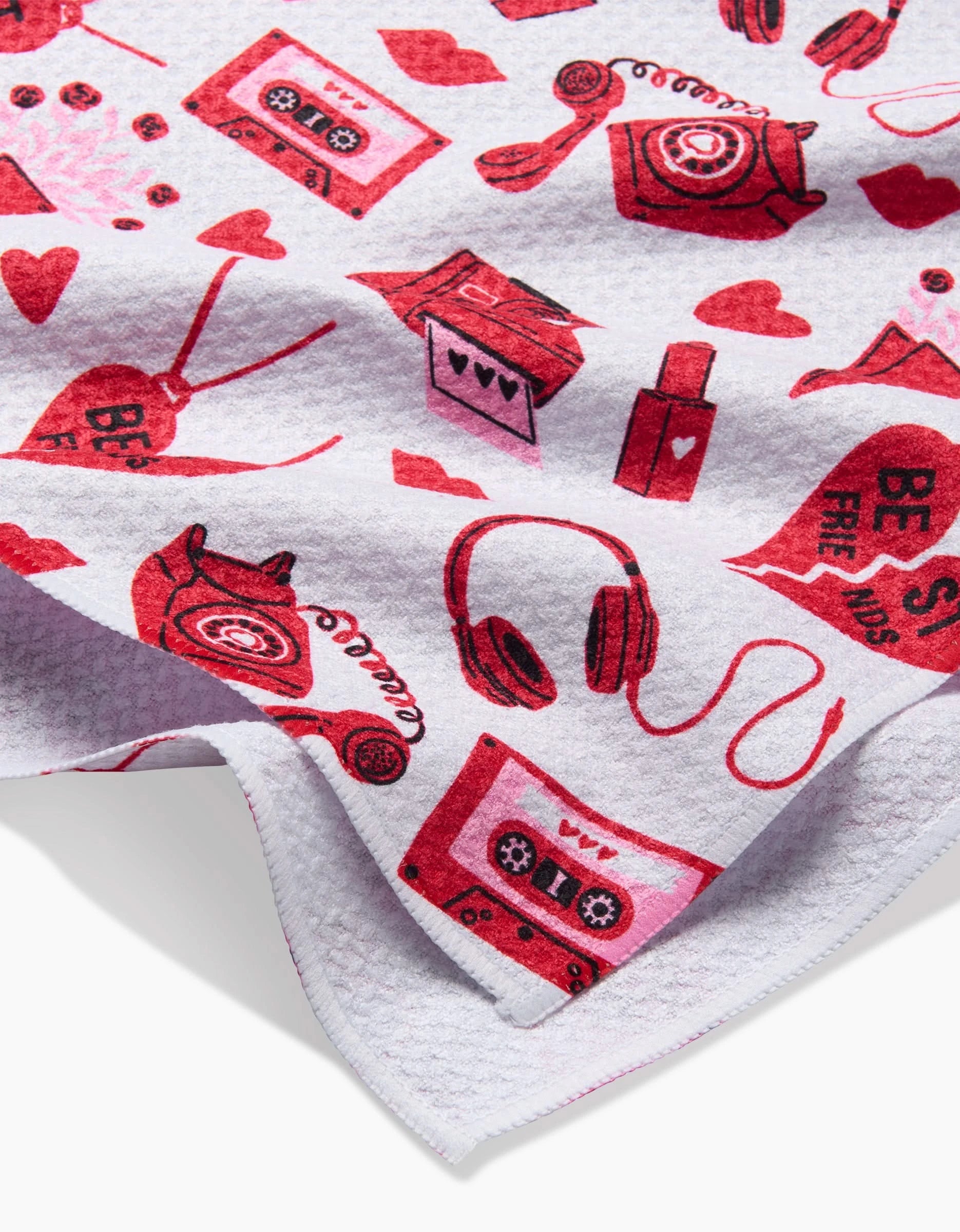 The Best Friends tea towel by Charlie Rowan Designs features a white textured fabric with red and pink vintage telephones, cassette tapes, headphones, hearts, and cheerful speech bubbles—a fun and practical kitchen accent.