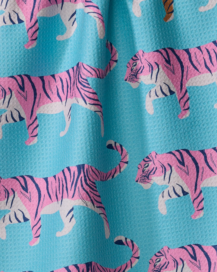 The Big Cats kitchen towel by Julianne Haness features a textured blue fabric with playful pink and purple tigers walking in a repeating pattern for a fun, colorful look.