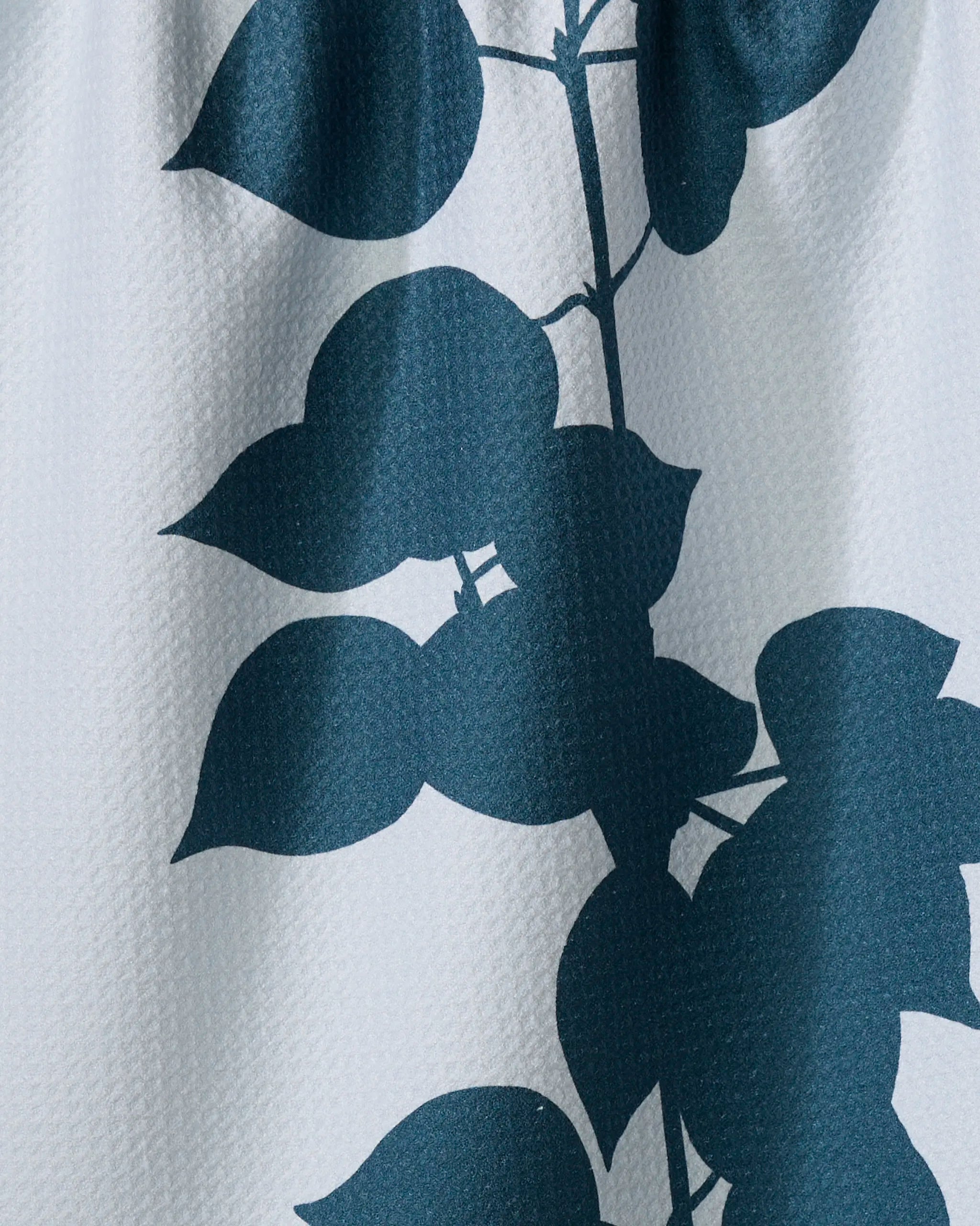 A close-up of the Birch absorbent dish towel by PrintedPlant, featuring a textured material with overlapping dark blue leafy patterns on a light background.