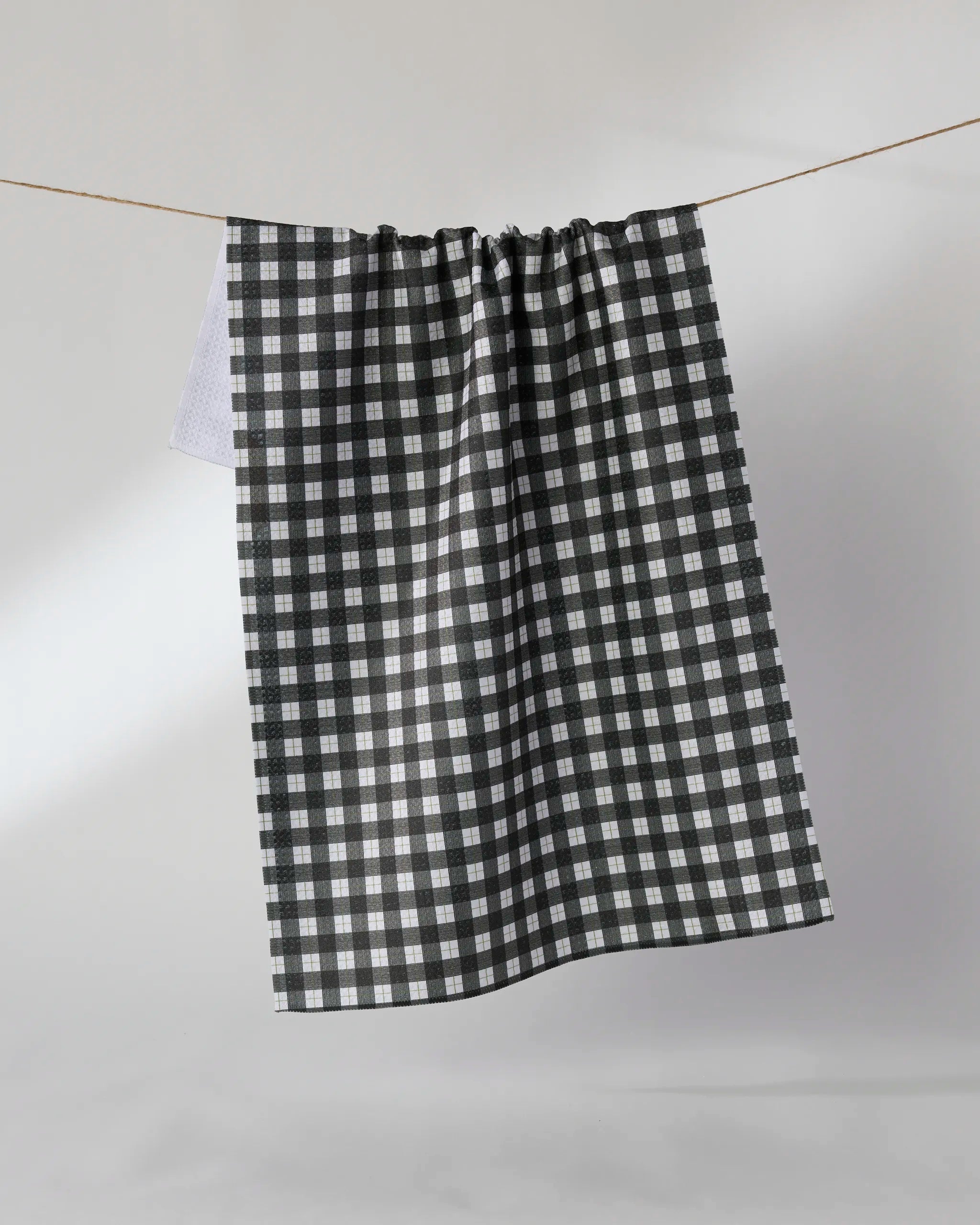 The Geometry Birchwood quick-drying towel, featuring a black and white checkered pattern, hangs on a thin clothesline against a light background.