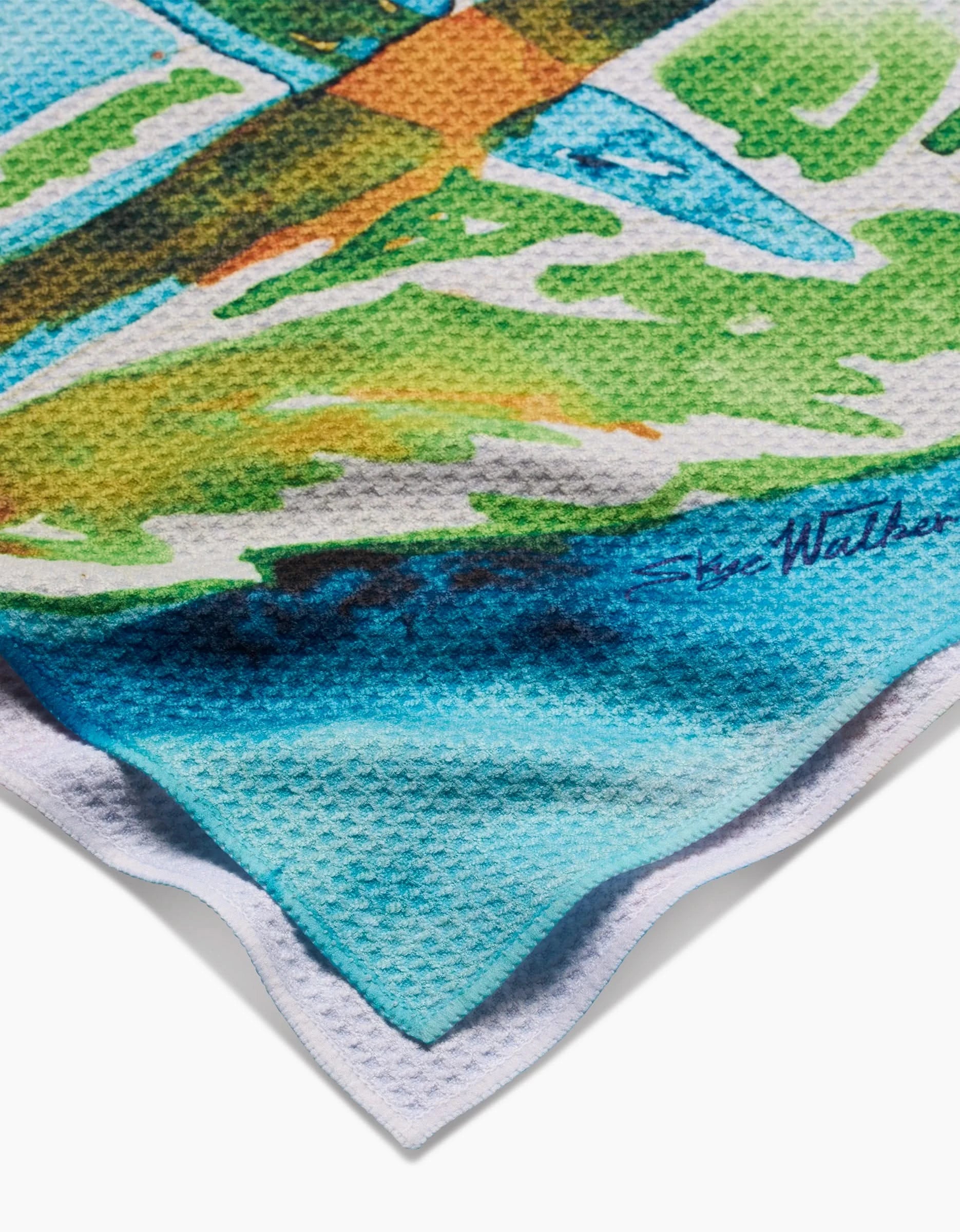 A close-up of the colorful, textured Geoweave™ fabric in the Skye Walker Bird Of Paradise Tea Towel, featuring a vibrant watercolor design and Skye Walkers signature near the edge.