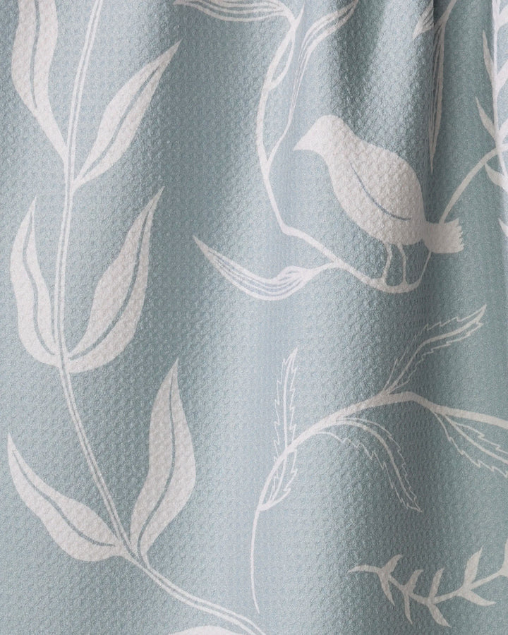 Birdsong by Elana Gabrielle is an eco-friendly, light blue textured kitchen towel with a minimalist white botanical and bird pattern featuring branches, leaves, and a perched bird.
