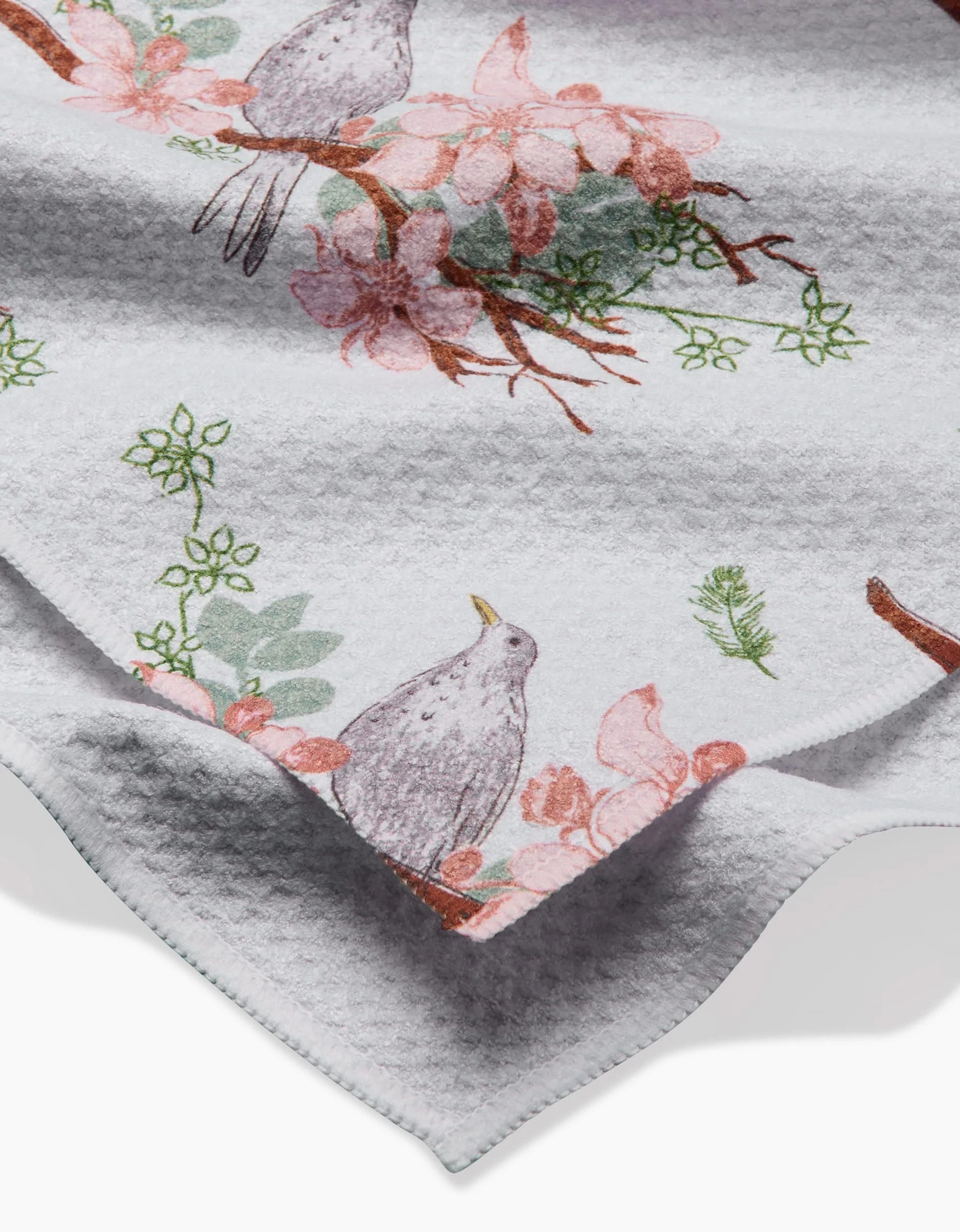 A close-up of the Linda Fox Blackbird and Blossom Geoweave fabric, featuring birds on branches amid pink flowers and green leaves.