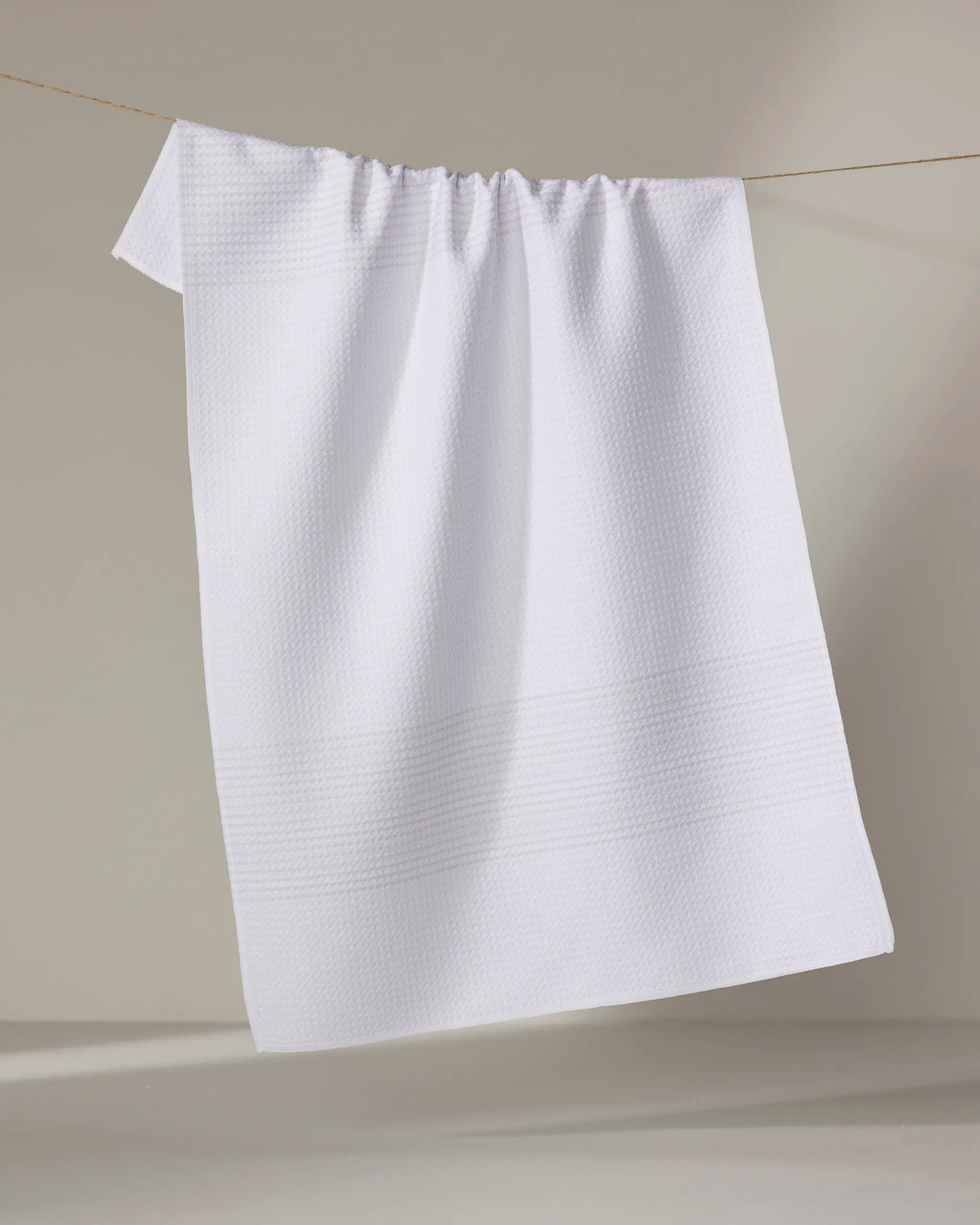 The Buy Guide's "Blank Space - Beige" kitchen towel hangs neatly on a thin line against a light background, highlighting its textured pattern and soft, absorbent fabric.