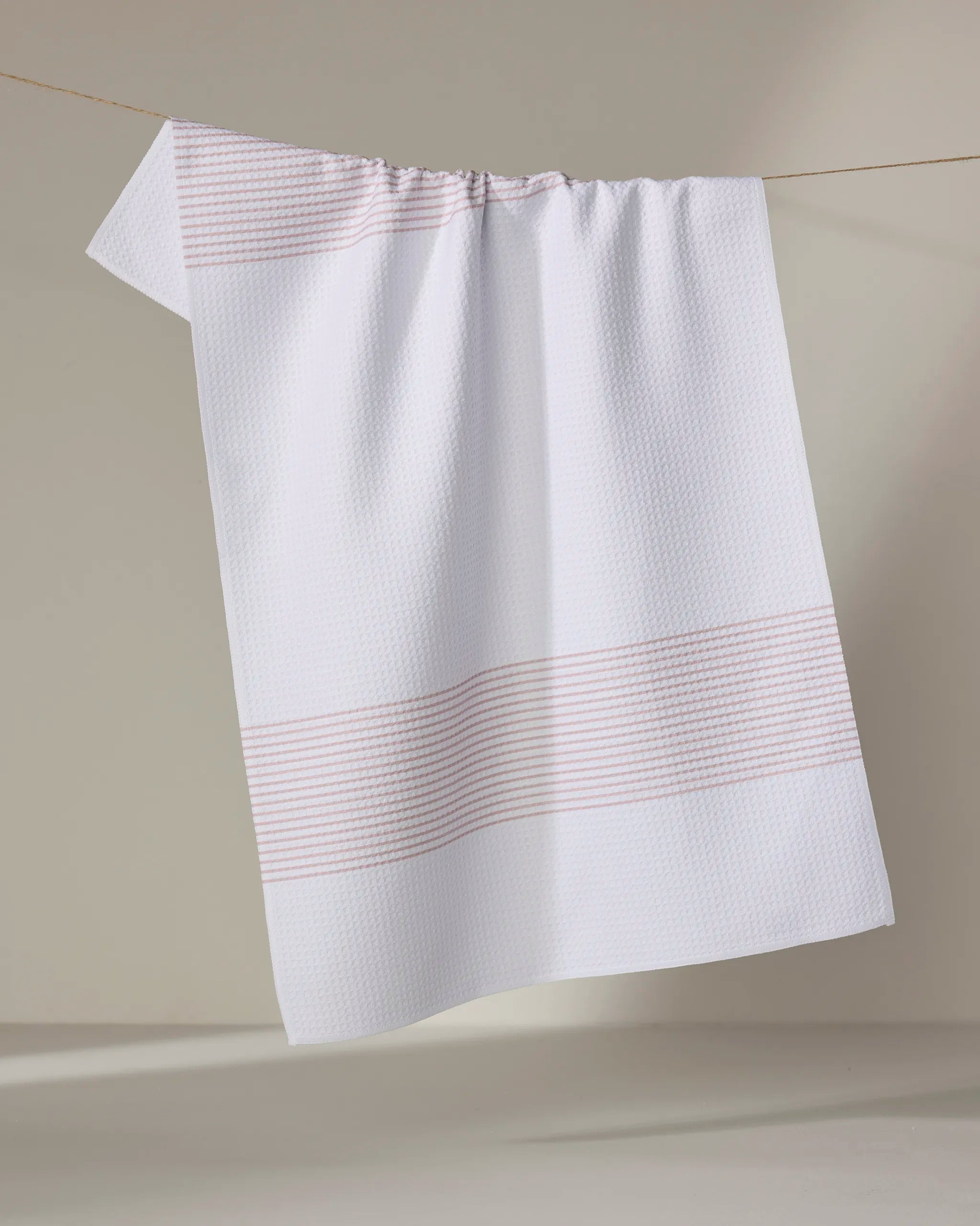The Buy Guide’s Blank Space - Dusty Rose textured absorbent kitchen towel with subtle beige stripes hangs on a string against a neutral background.