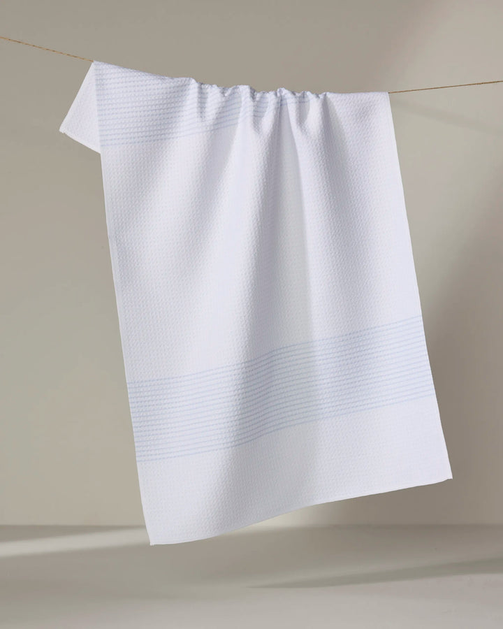 The Buy Guide’s Blank Space - Light Blue tea towel, made from ultra-absorbent recycled materials, features a subtle texture with faint blue stripes and hangs neatly over a clothesline against a neutral background.