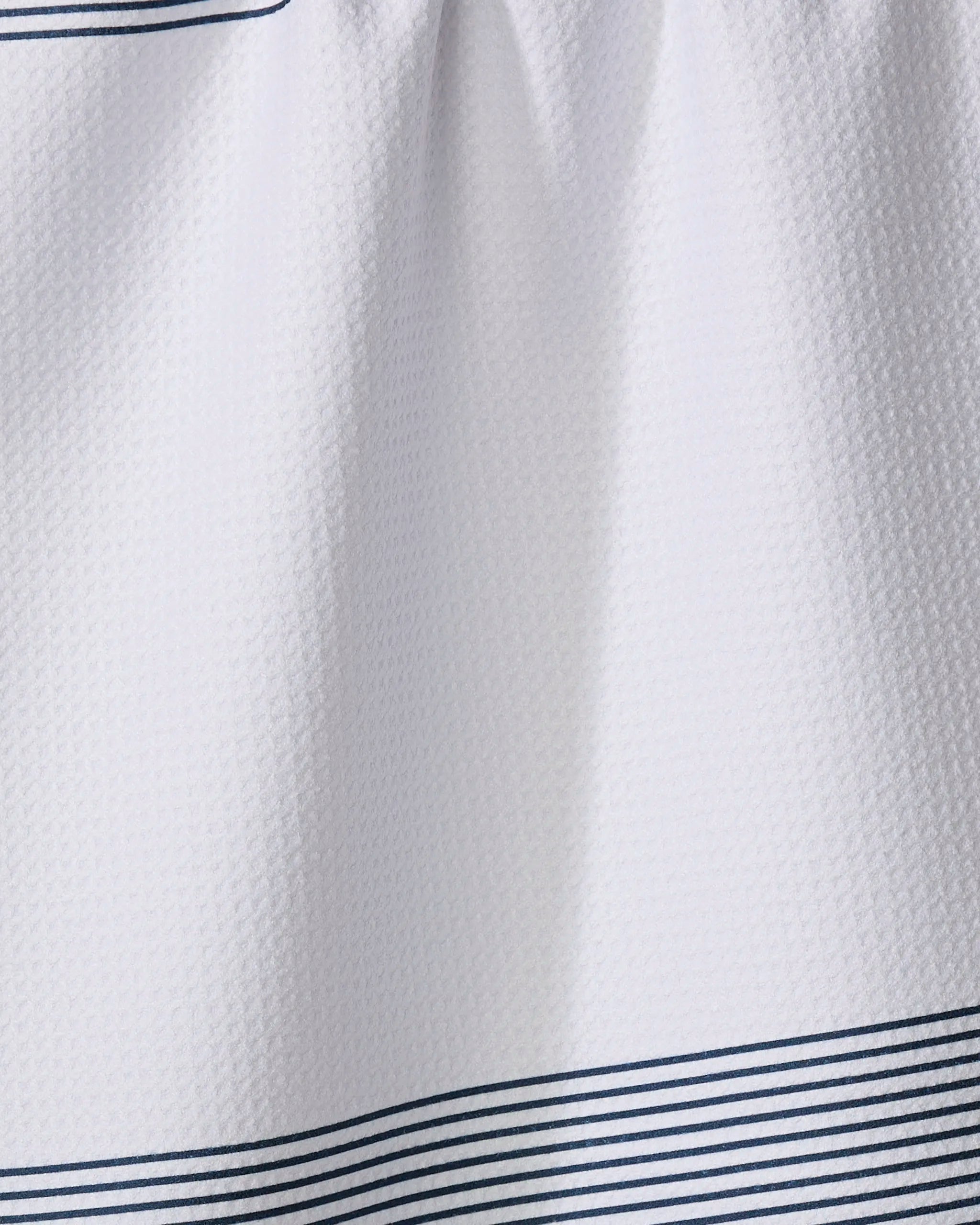 Close-up of "Blank Space - Navy" by The Buy Guide, a white textured kitchen tea towel featuring thin, evenly spaced horizontal navy blue stripes near the bottom edge. Made from recycled materials for an eco-friendly touch.