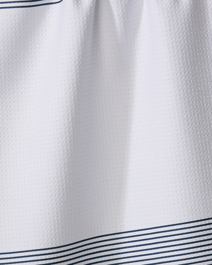 Close-up of "Blank Space - Navy" by The Buy Guide, a white textured kitchen tea towel featuring thin, evenly spaced horizontal navy blue stripes near the bottom edge. Made from recycled materials for an eco-friendly touch.
