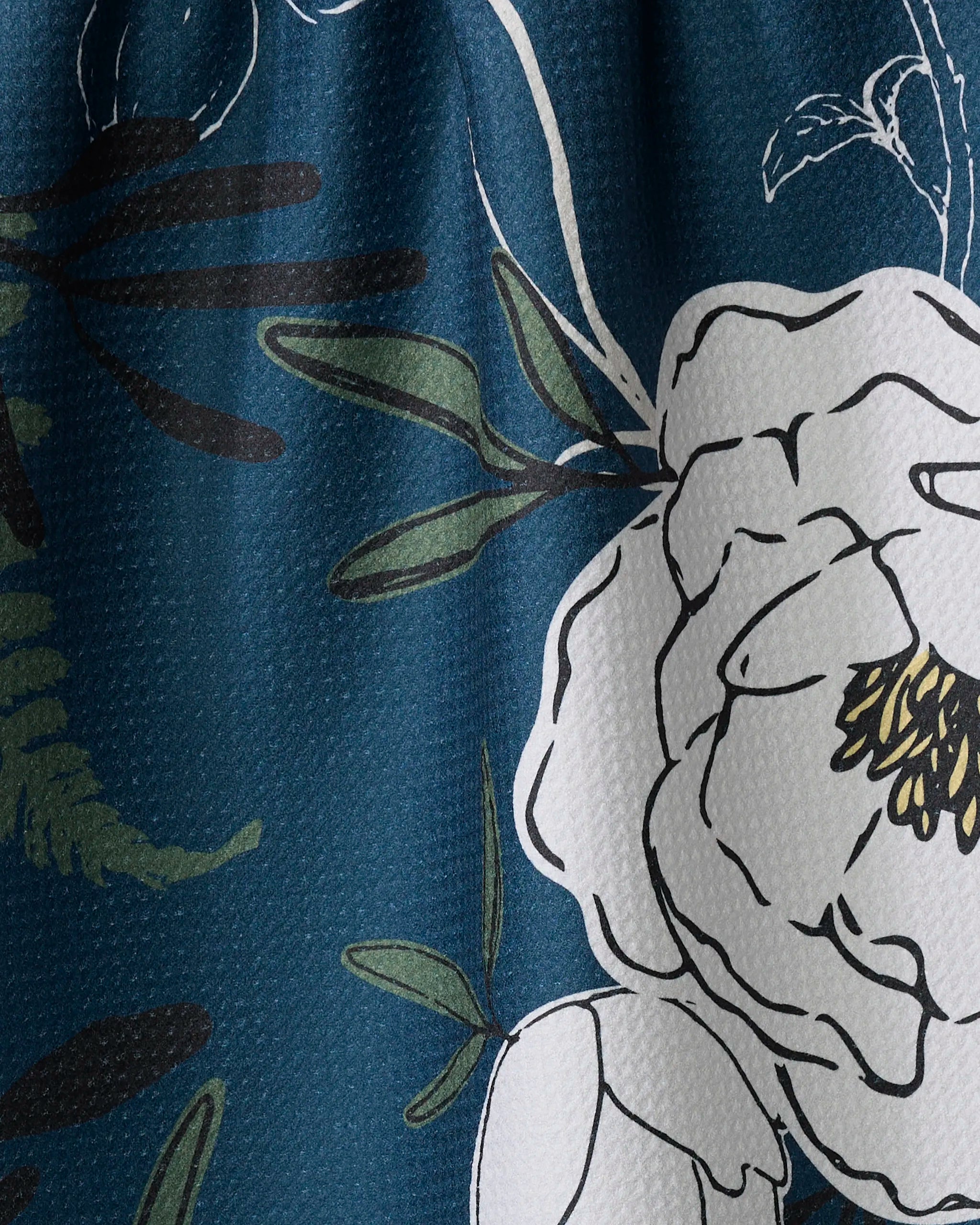 A close-up of the Blooming Possibilities tea towel by Ashley Celena, showing its blue Geoweave fabric with a textured surface, white floral pattern, and green leafy accents outlined in black.