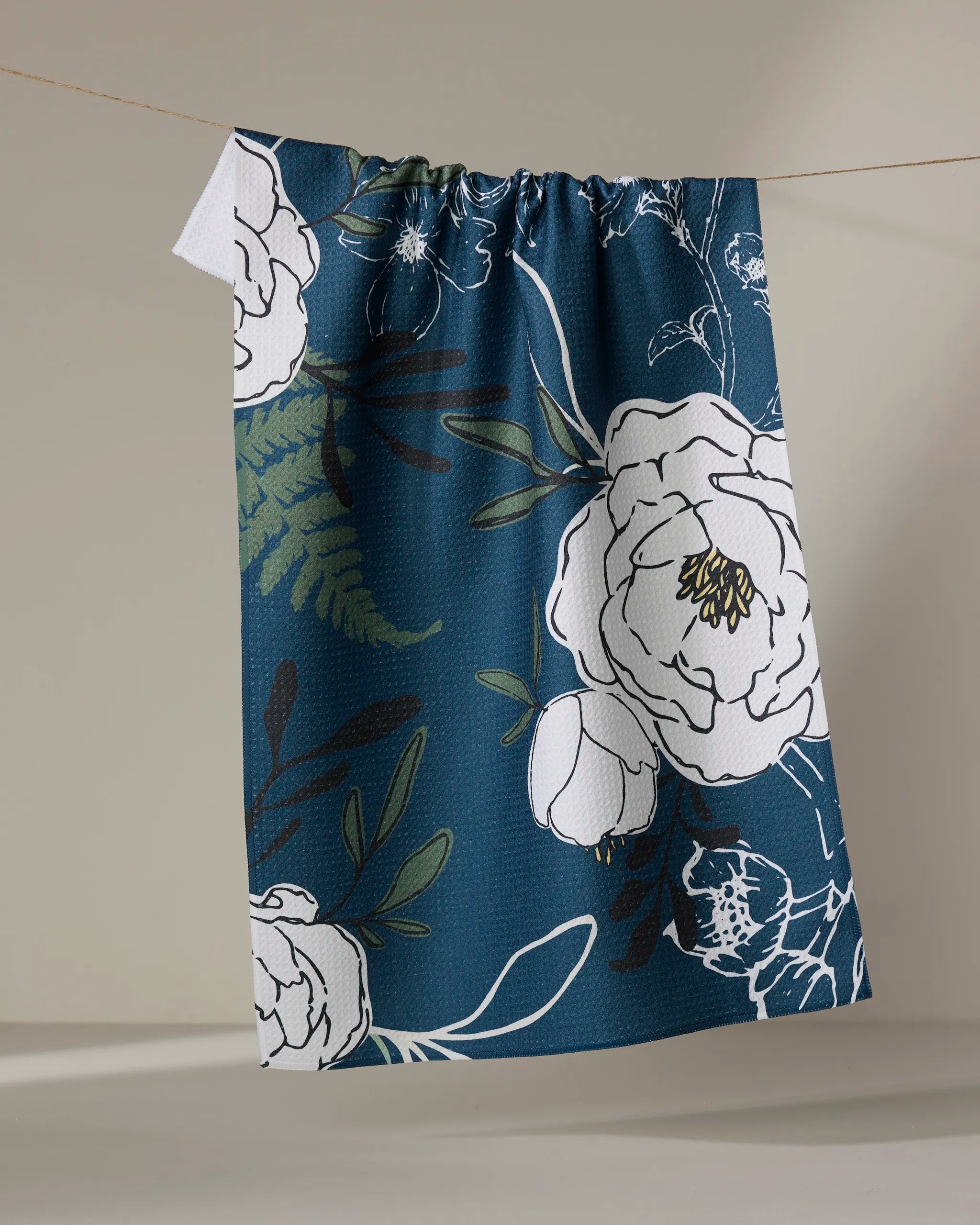 The "Blooming Possibilities" curtain by Ashley Celena features bold white florals and green leaves on blue recycled fabric, hanging from a rope against a beige backdrop.