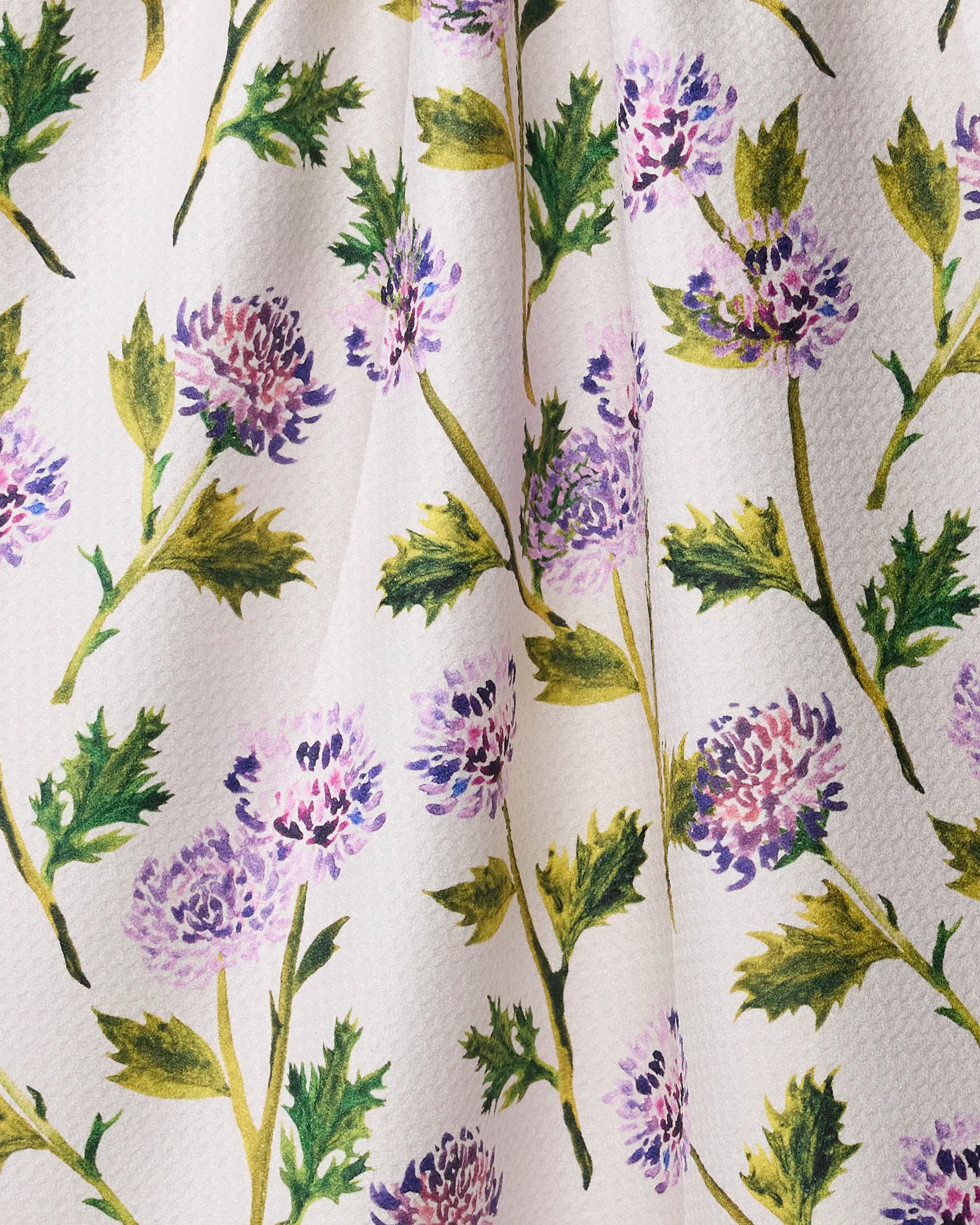Close-up of Geometry’s Blooming Thistle Kitchen Tea Towel, crafted from recycled Geoweave fabric with a hand-painted watercolor print of purple thistle flowers and green leaves.