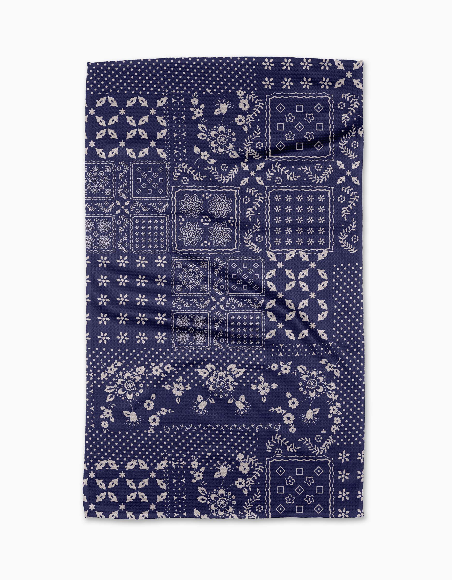 The Blossoming Bandanna Blue tea towel by Geometry features a dark blue rectangular design with white floral and geometric patchwork, arranged in a quilt-like style. Made from recycled materials for eco-friendly appeal.