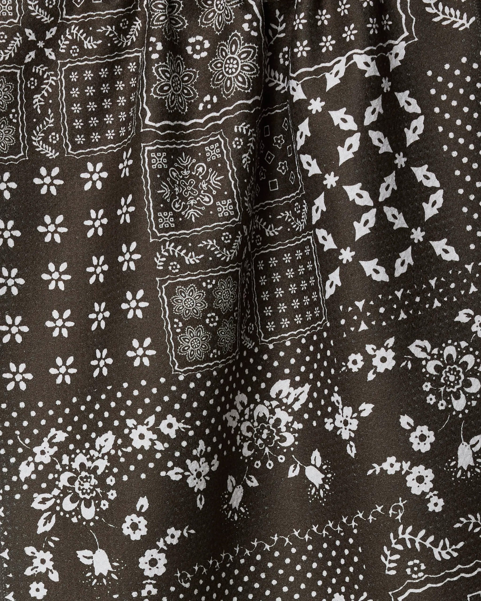 A close-up of Geometry's Blossoming Bandanna Brown, a dark fabric with a white bandana-style floral and geometric pattern—an eco-friendly kitchen or tea towel that adds modern style to your home.