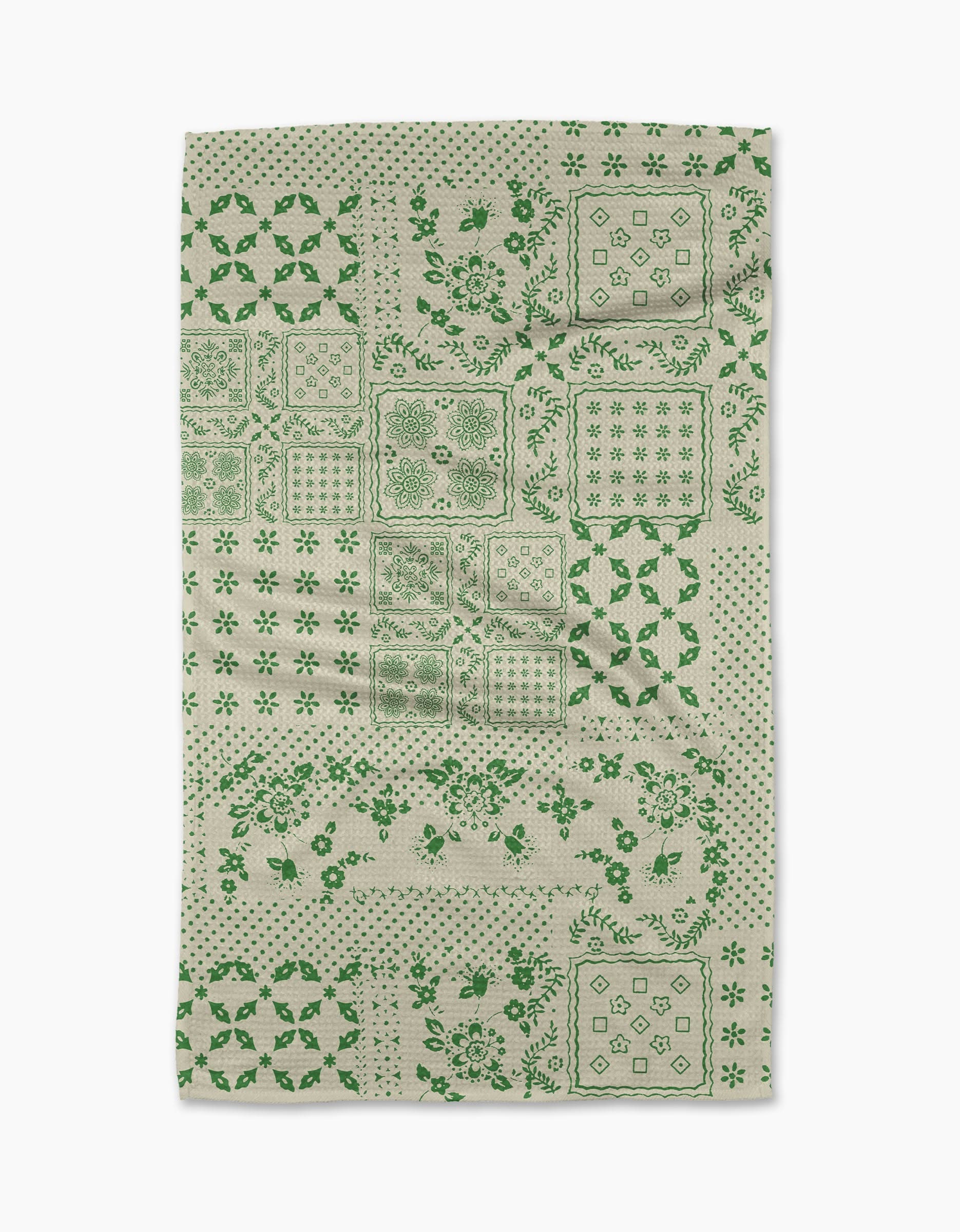 The Blossoming Bandanna Green tea towel by Geometry features a patchwork of green floral and geometric designs in squares and rectangles on an off-white background.