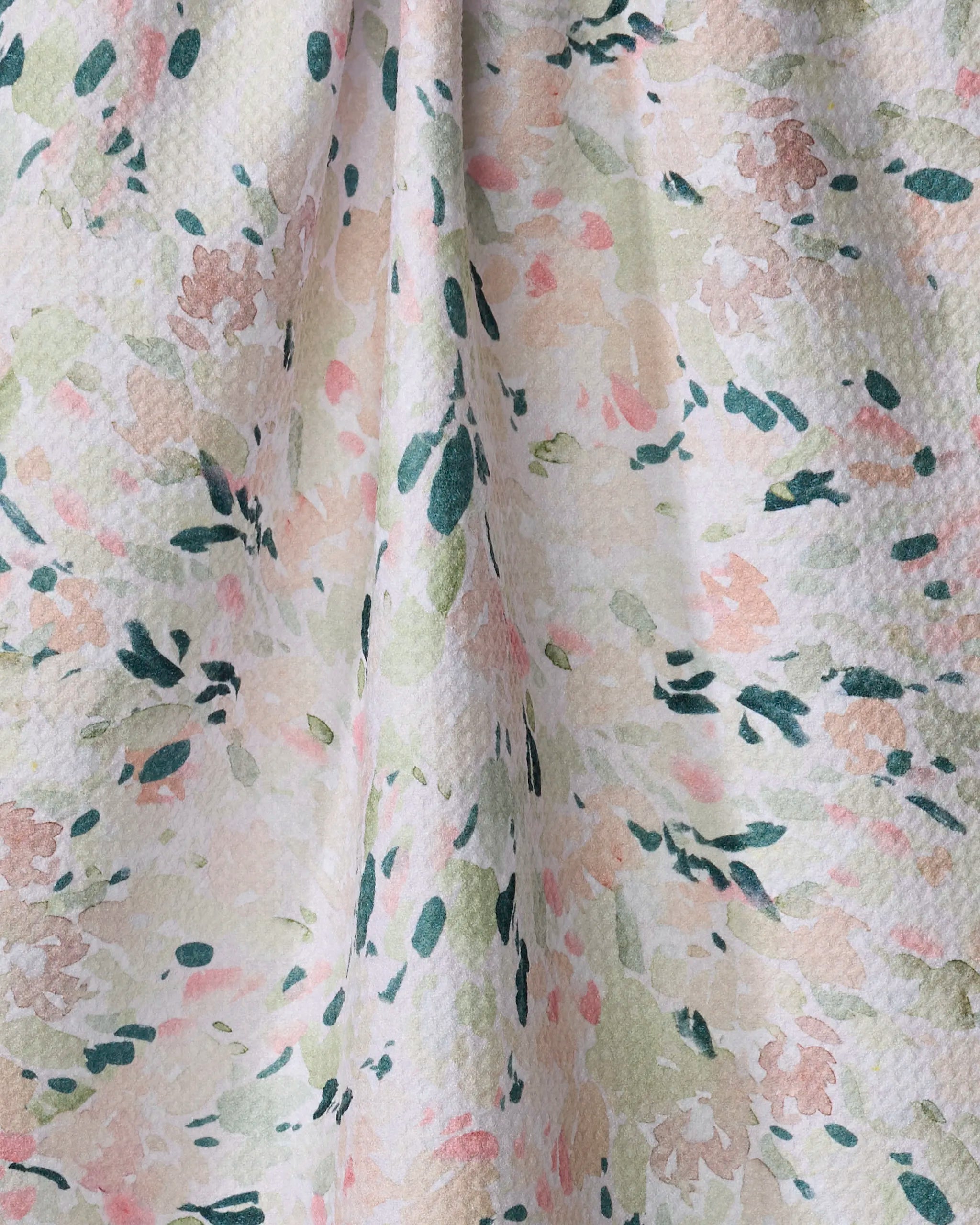 A close-up of Anee Shah's Blossoms tea towel, ultra-absorbent and made from recycled materials, displays a soft pastel floral pattern in green, peach, pink, and cream with abstract leaves adding delicate texture.