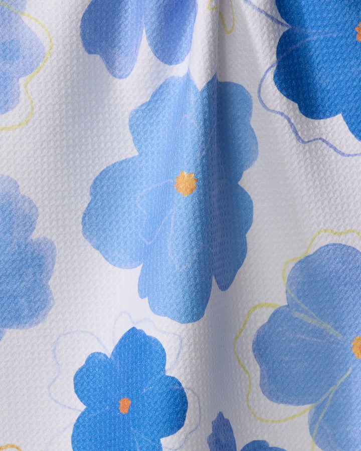 The Blue Blossoms kitchen towel by Elana Gabrielle is a white, textured towel made from recycled materials, featuring large blue flowers with yellow centers and light blue floral outlines.