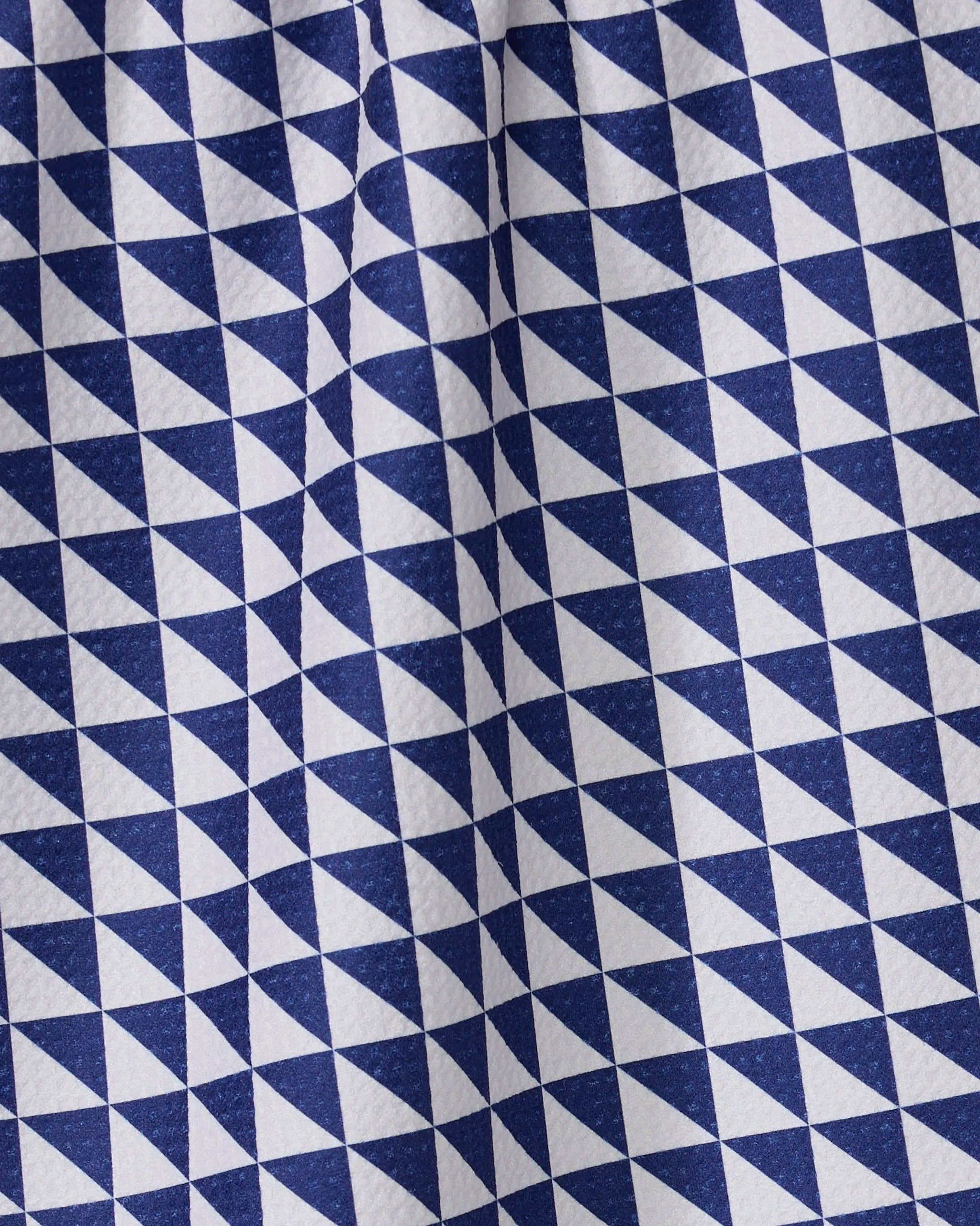 The Geometry Blue Whirl tea towel features a blue and white geometric triangle pattern for an optical effect. Made from recycled materials, this quick-drying towel has visible texture and folds.