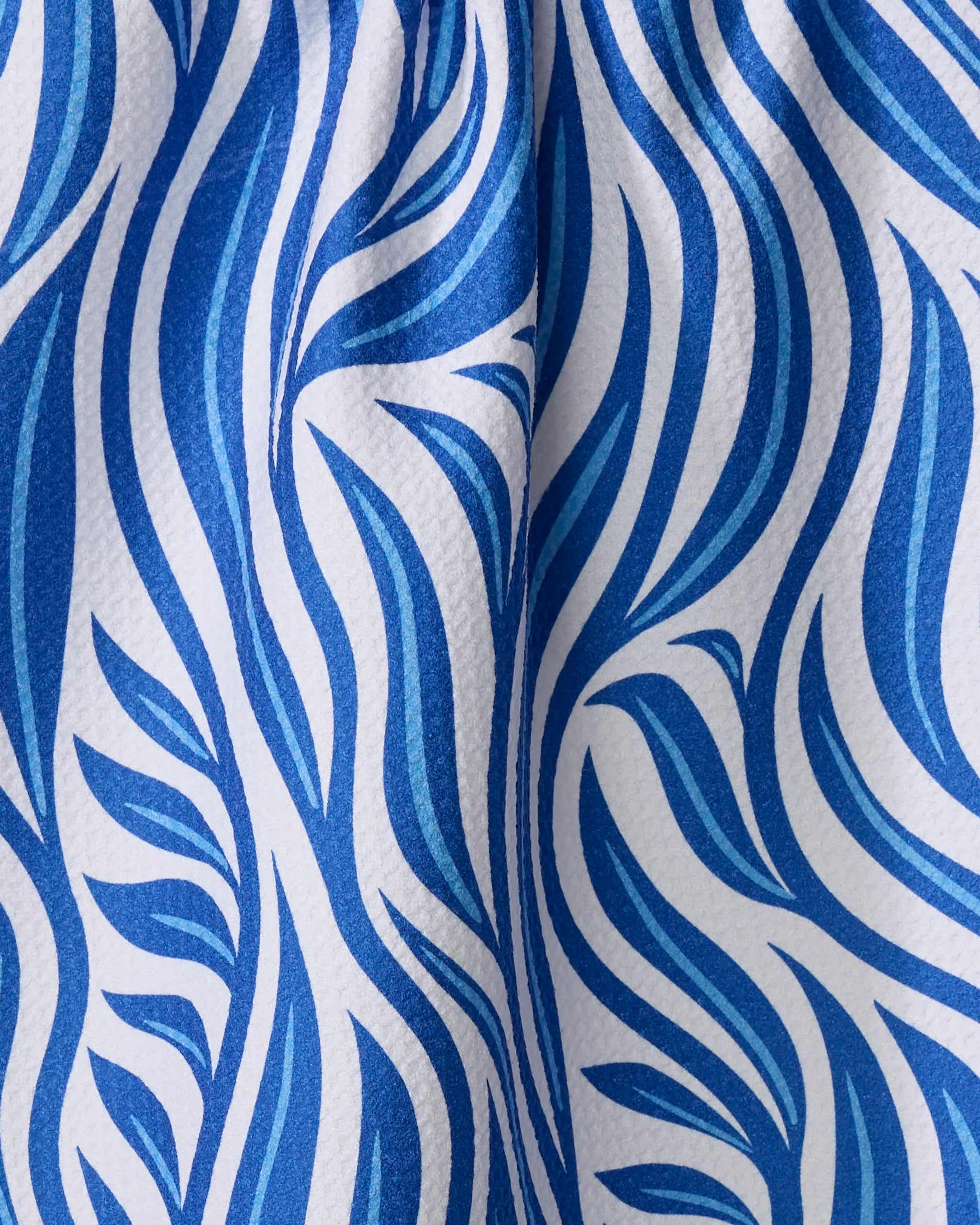 The Rachel Parker Blue Willow Wave tea towel features bold blue, wave-like lines on textured white, bringing a dynamic and stylish touch to your kitchen.