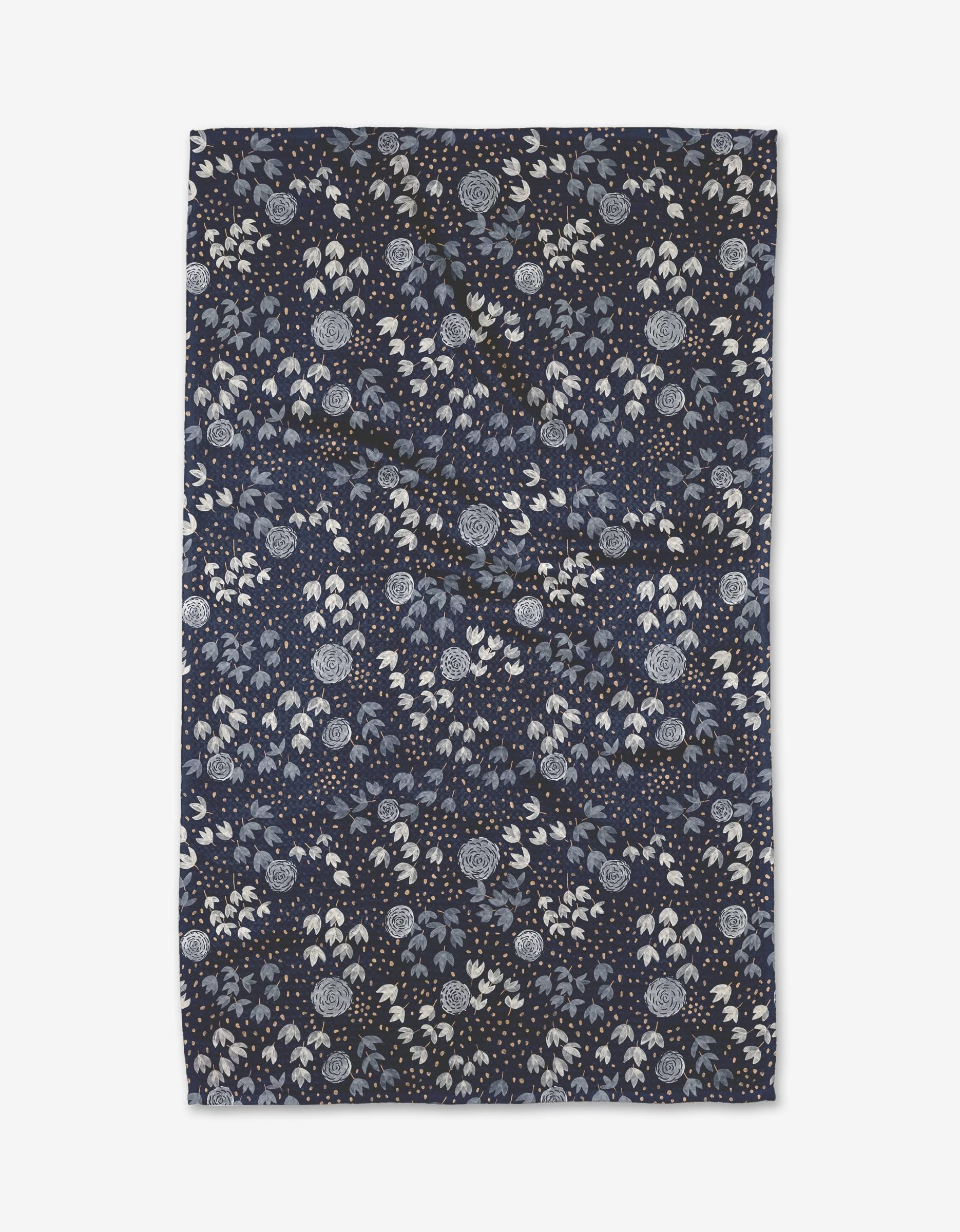 The Blue Winter Petal tea towel by Katie OShea features a dark blue background with a dense pattern of white and light blue flowers, leaves, and dots. Made from quick-drying recycled materials, it combines botanical beauty with eco-friendly design.