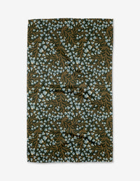 The Bluewood Garden tea towel by Danelys Sidron features a dark background with brown leaves and light blue floral clusters in a botanical pattern, crafted from recycled materials.
