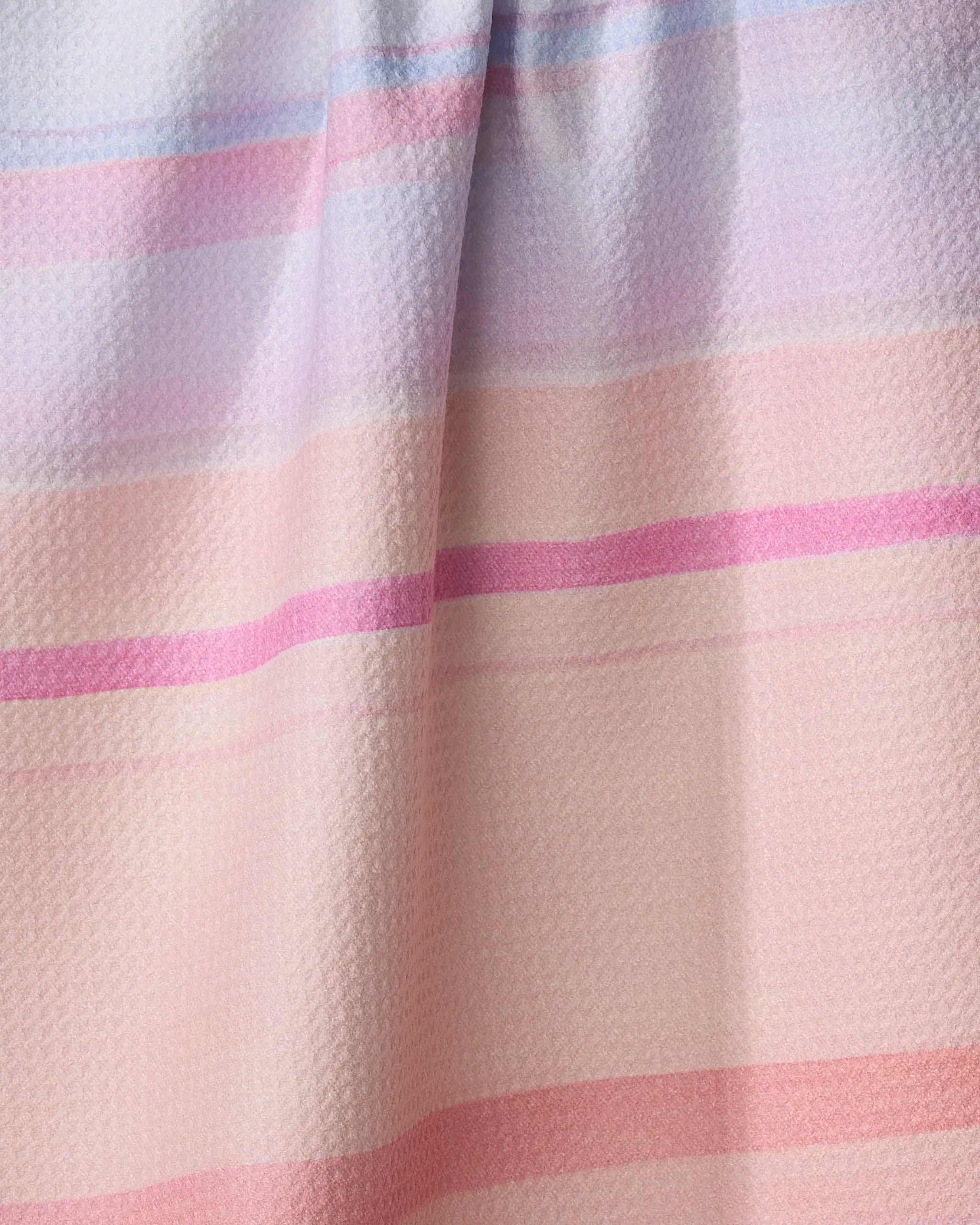 A close-up of the Stefanie Bales "Blush" tea towel, showcasing textured fabric with horizontal pastel stripes in pink, peach, and lavender hues, and a subtle vertical fold at the center.