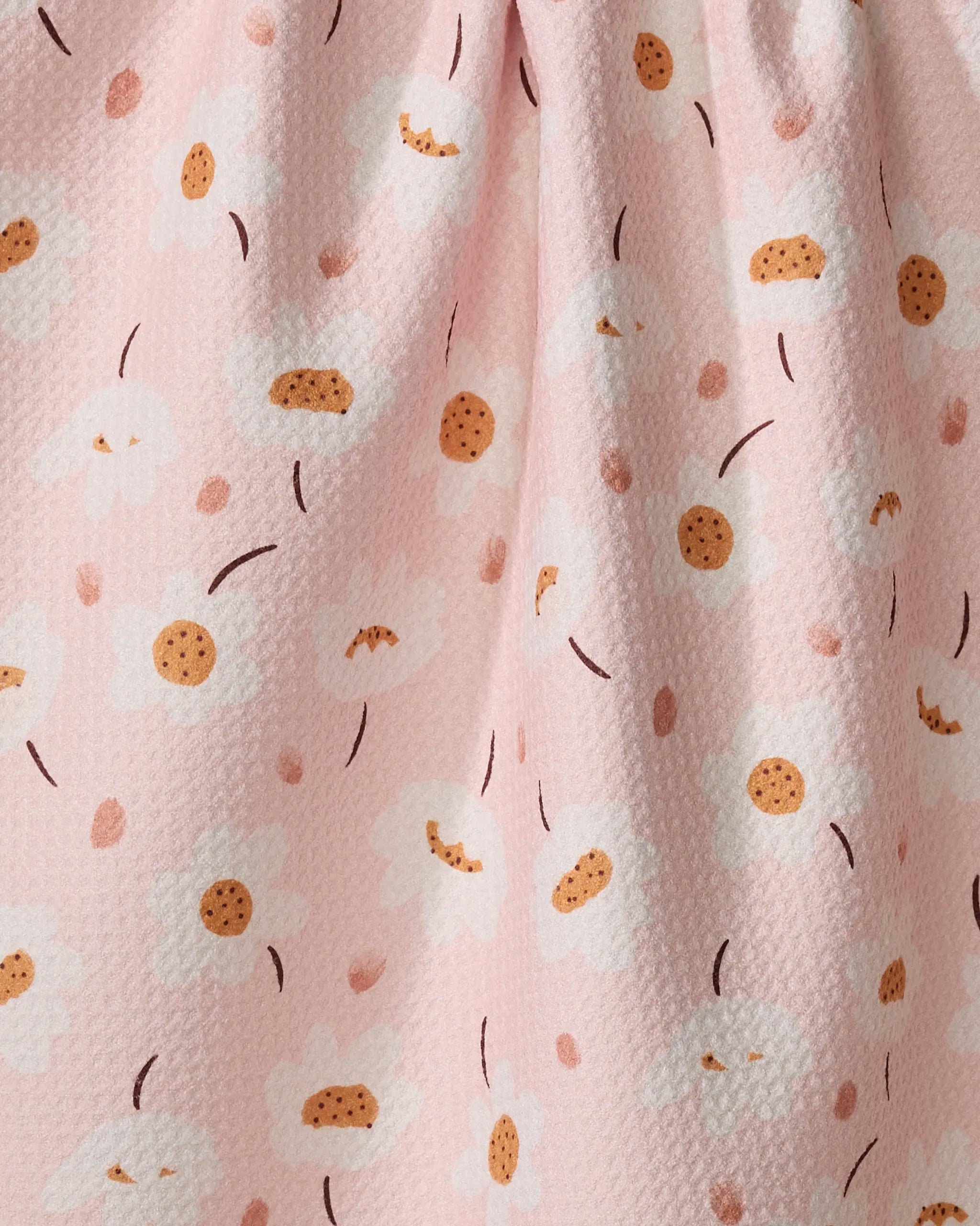 A close-up of Blush Meadows by Sara Mari, an ultra-absorbent towel in pink with textured fabric, adorned with simple white daisies featuring yellow centers and scattered brown lines and dots.