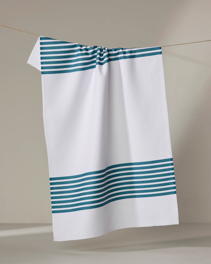 The Buy Guide’s Bold Blank Space - Emerald is a white ultra-absorbent tea towel with textured fabric and horizontal emerald stripes at the top and bottom, shown hanging from a clothesline against a neutral background.