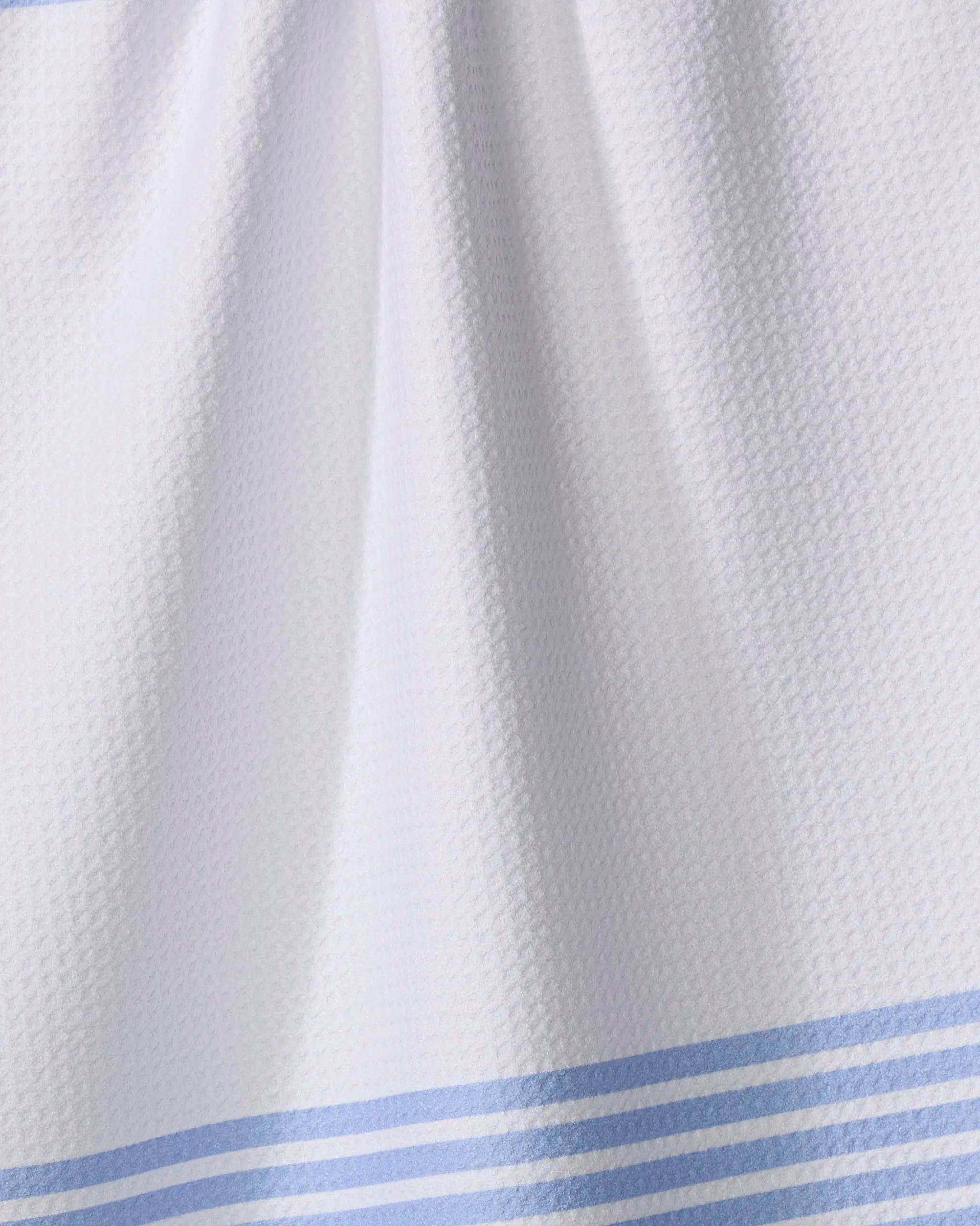A close-up of The Buy Guide's Bold Blank Space - French Blue tea towel, featuring white textured fabric with French blue stripes along the bottom and soft folds that highlight its ultra-absorbent finish.