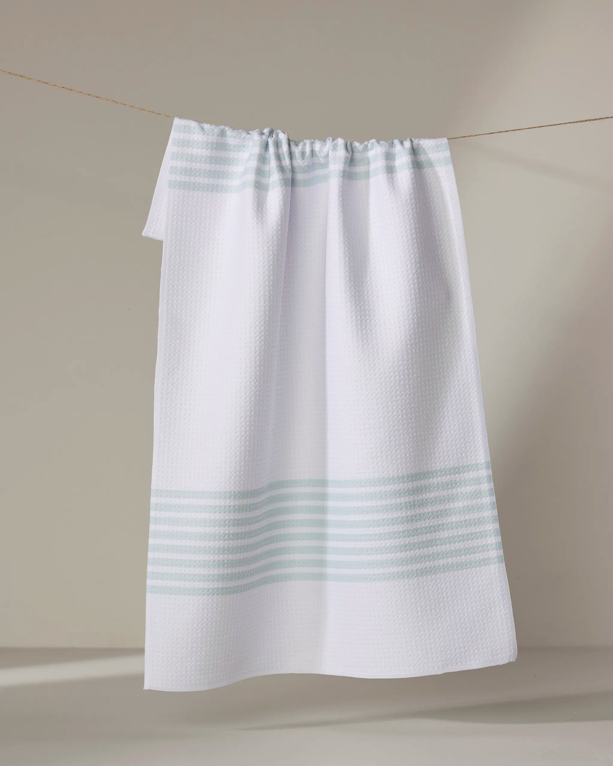 The Buy Guide’s Bold Blank Space - Mint tea towel, crafted from ultra-absorbent recycled materials with light blue stripes, hangs on a clothesline against a neutral background.